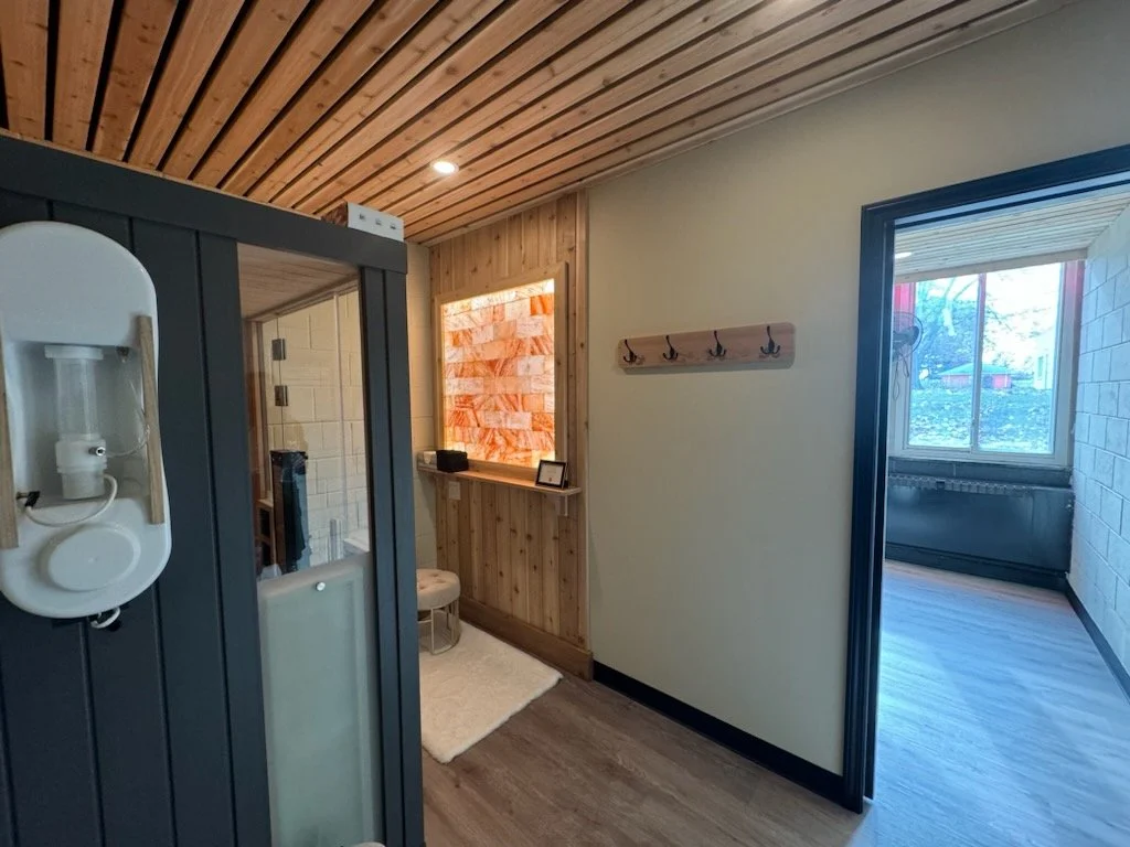 Interior of a small room with wooden ceiling and walls, a coat rack on the wall, and a sliding door leading to a room with large windows and a view outside.