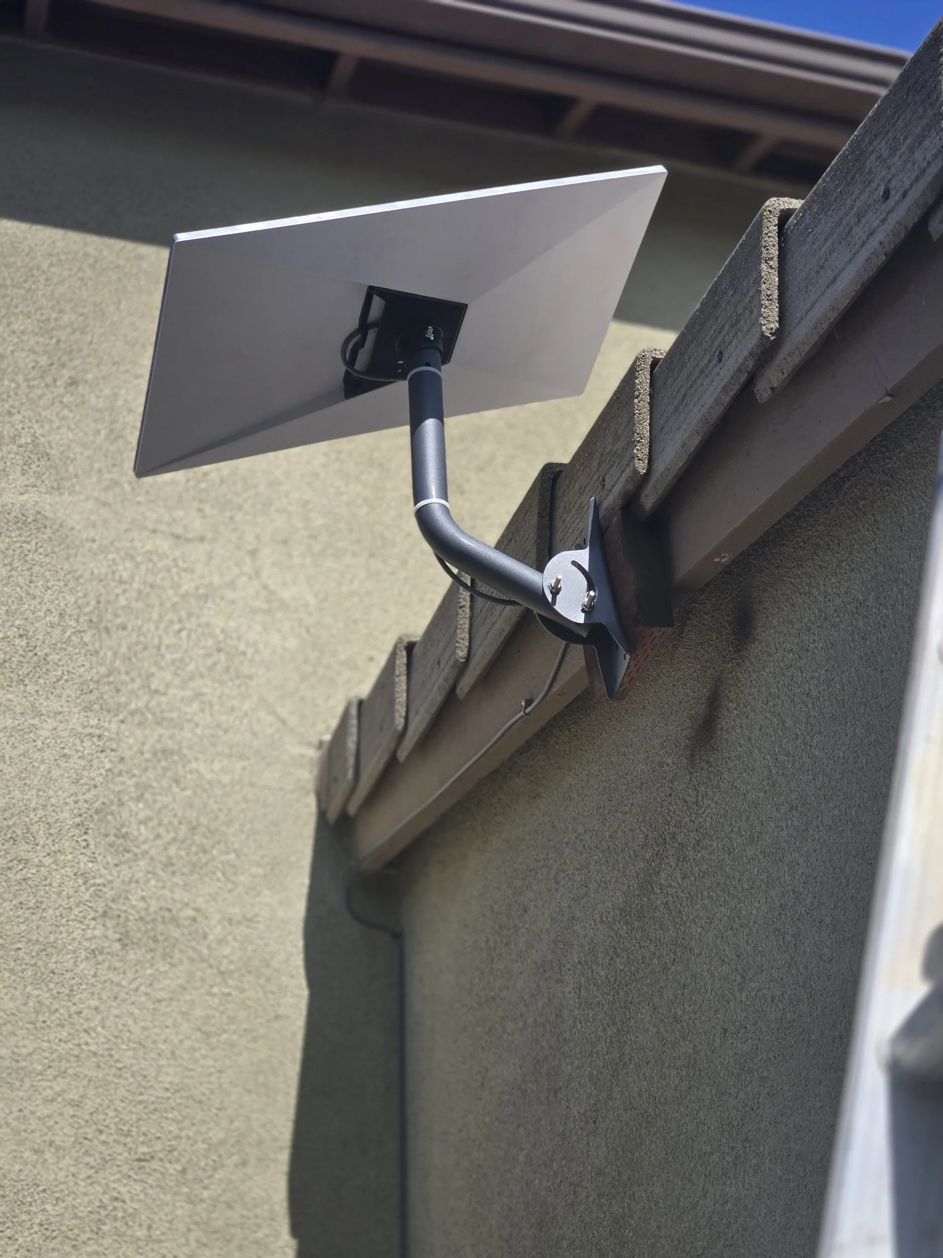 A satellite dish mounted on a wall next to a wooden ledge, with a blue sky in the background.