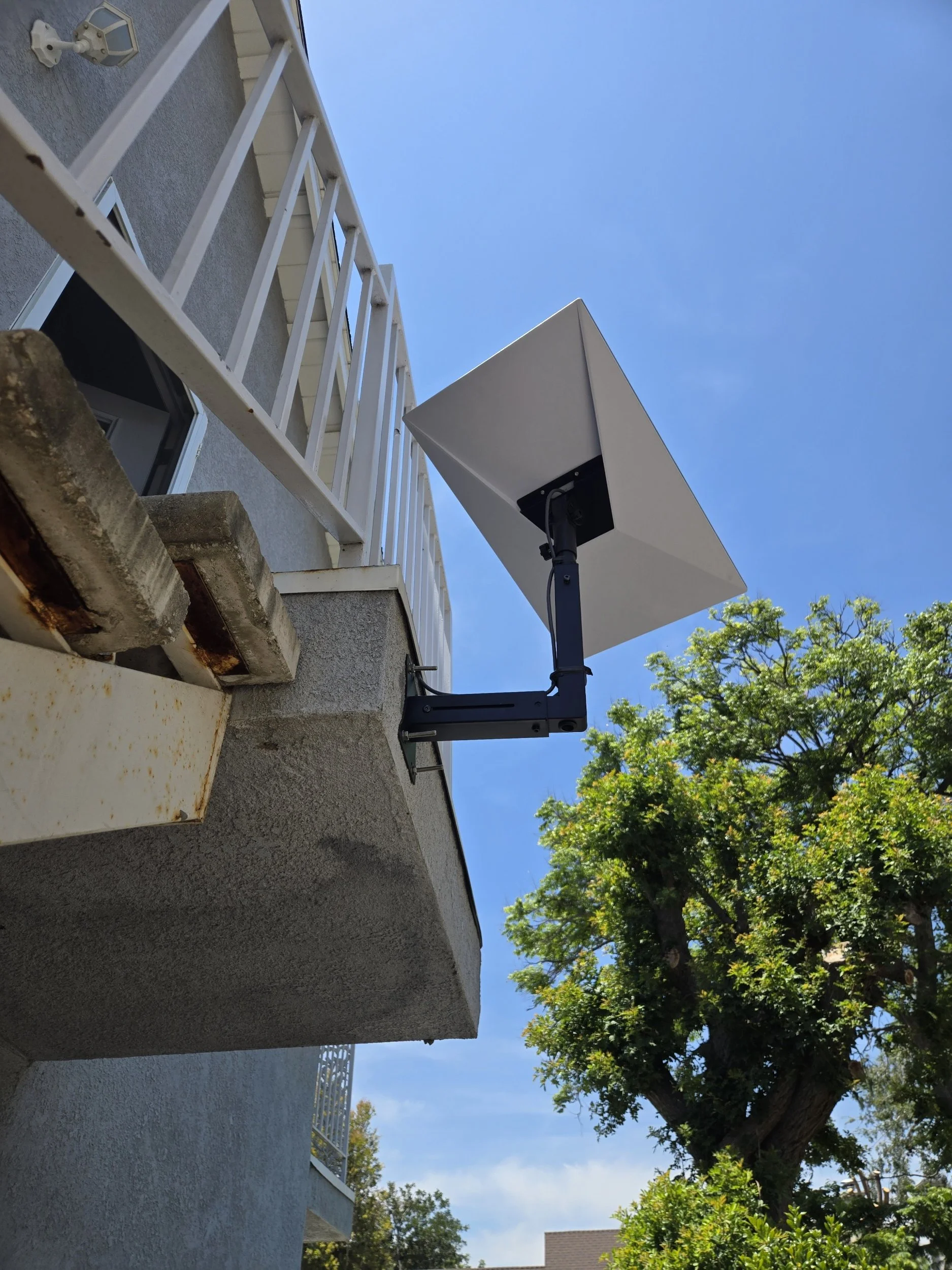 View of a building with a balcony, satellite dish, and a tree with green leaves under a clear blue sky.