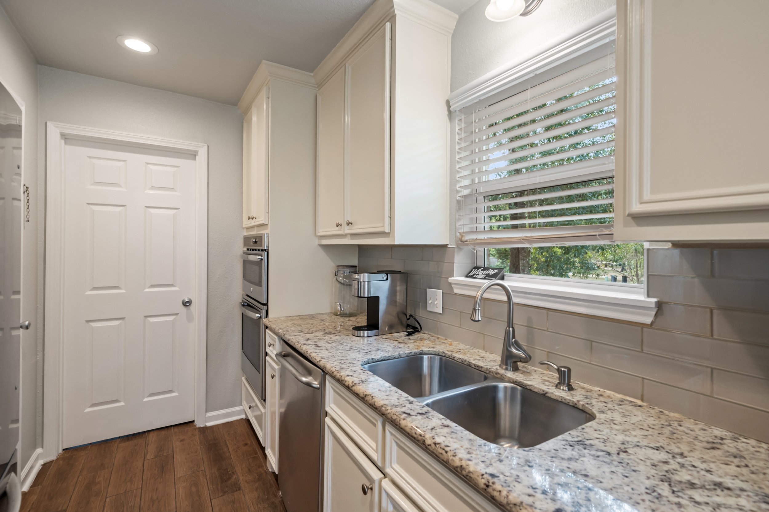 Kitchen with white cabinets, a window with blinds, granite countertop, stainless steel sink, and a coffee machine.