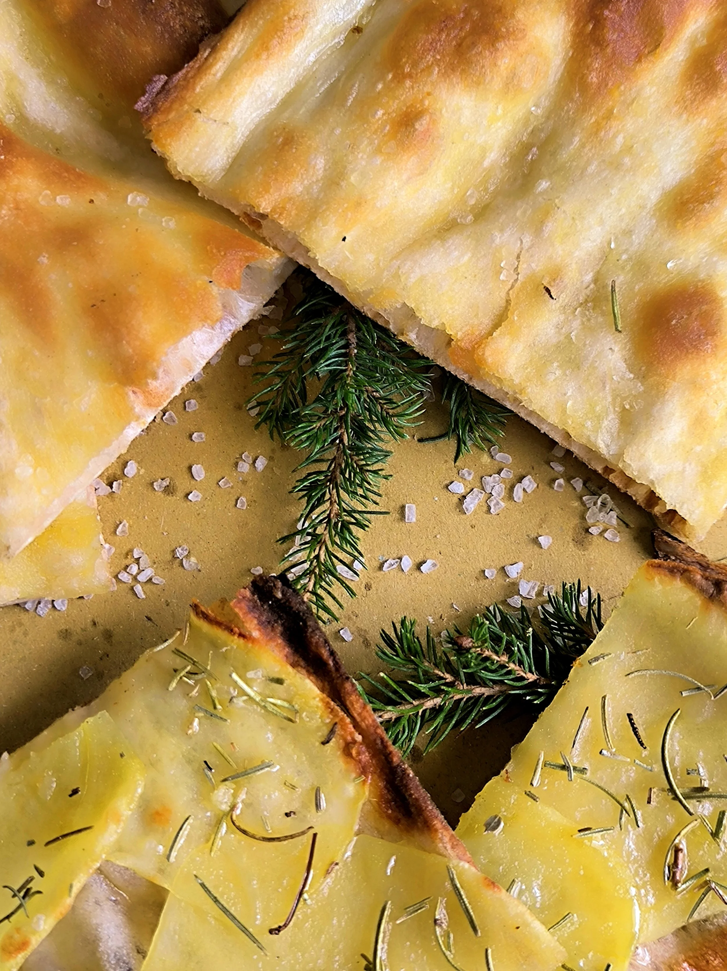 Fetta di focaccia con rosmarino e sale grosso, decorata con rametti di rosmarino.