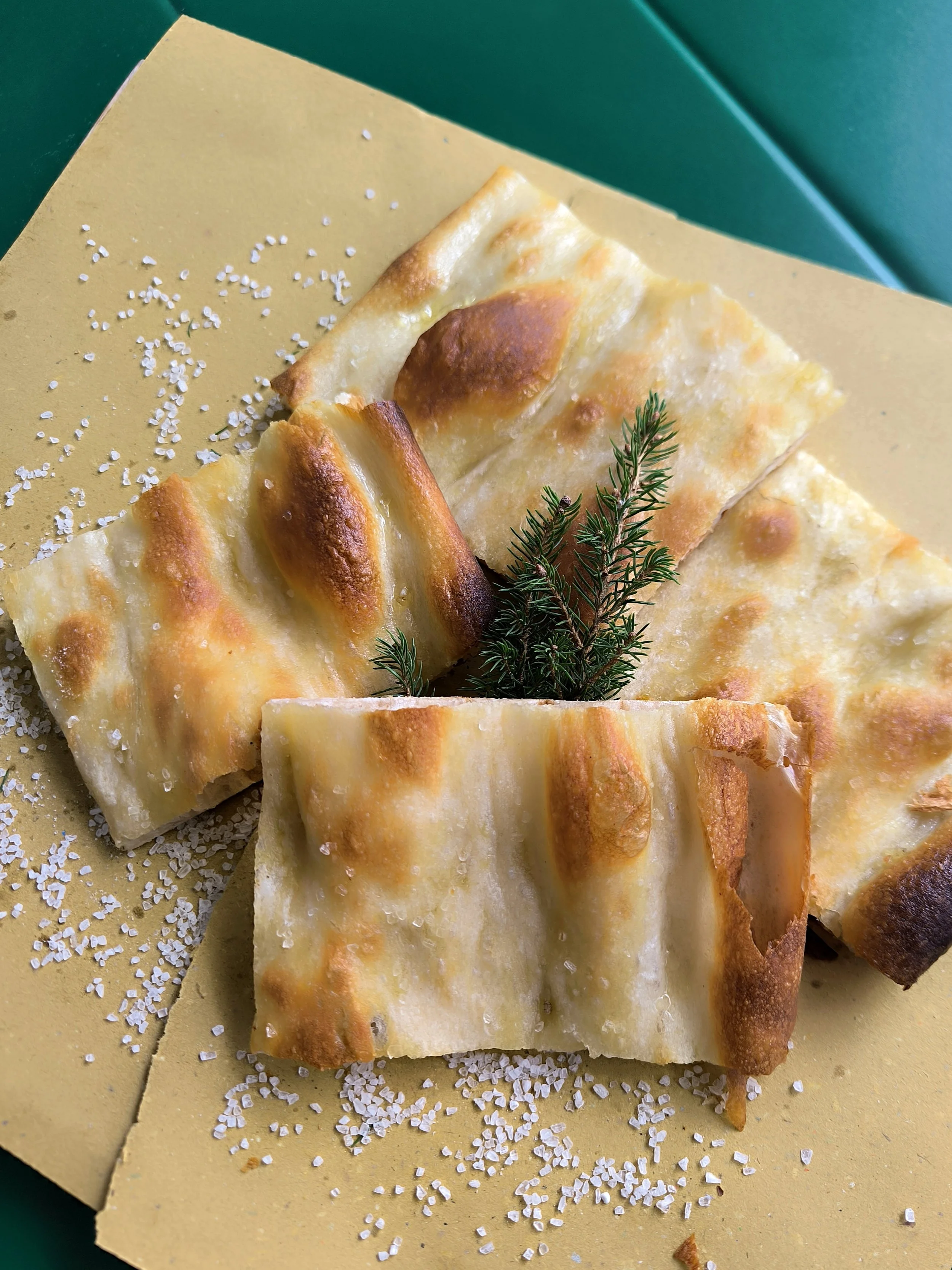 Fetta di pizza bianca senza farcitura con sale grosso e rametto di rosmarino.
