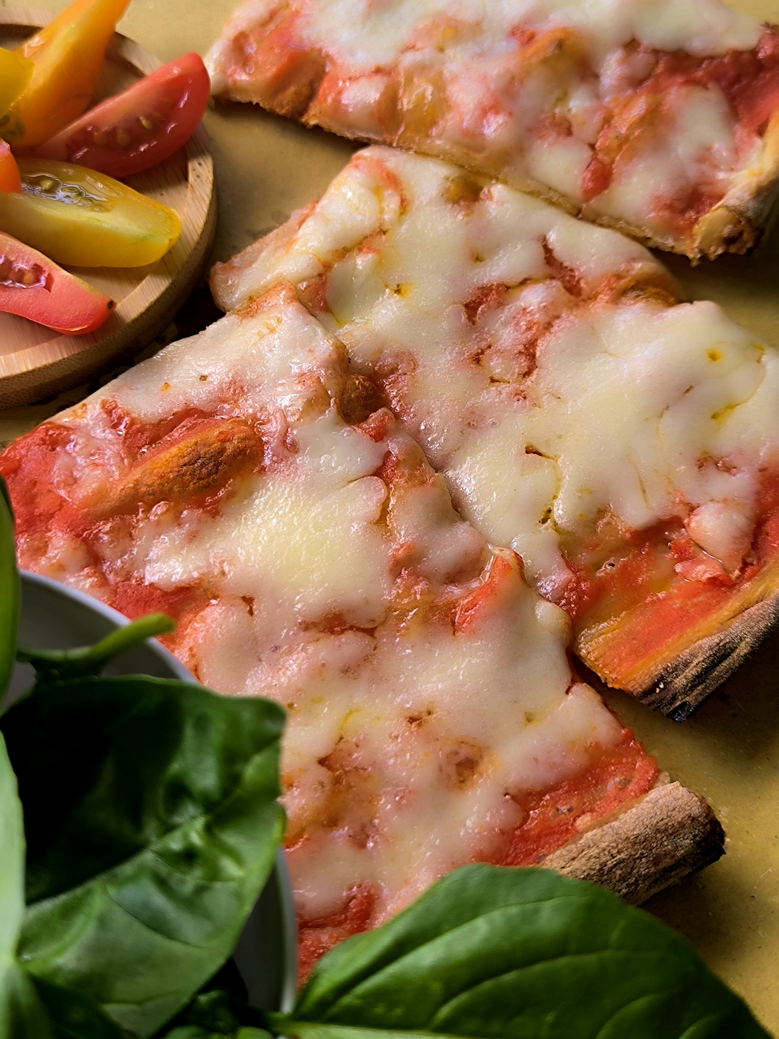 Pizza margherita con formaggio e pomodoro, accanto a verdure fresche come pomodorini e insalata.