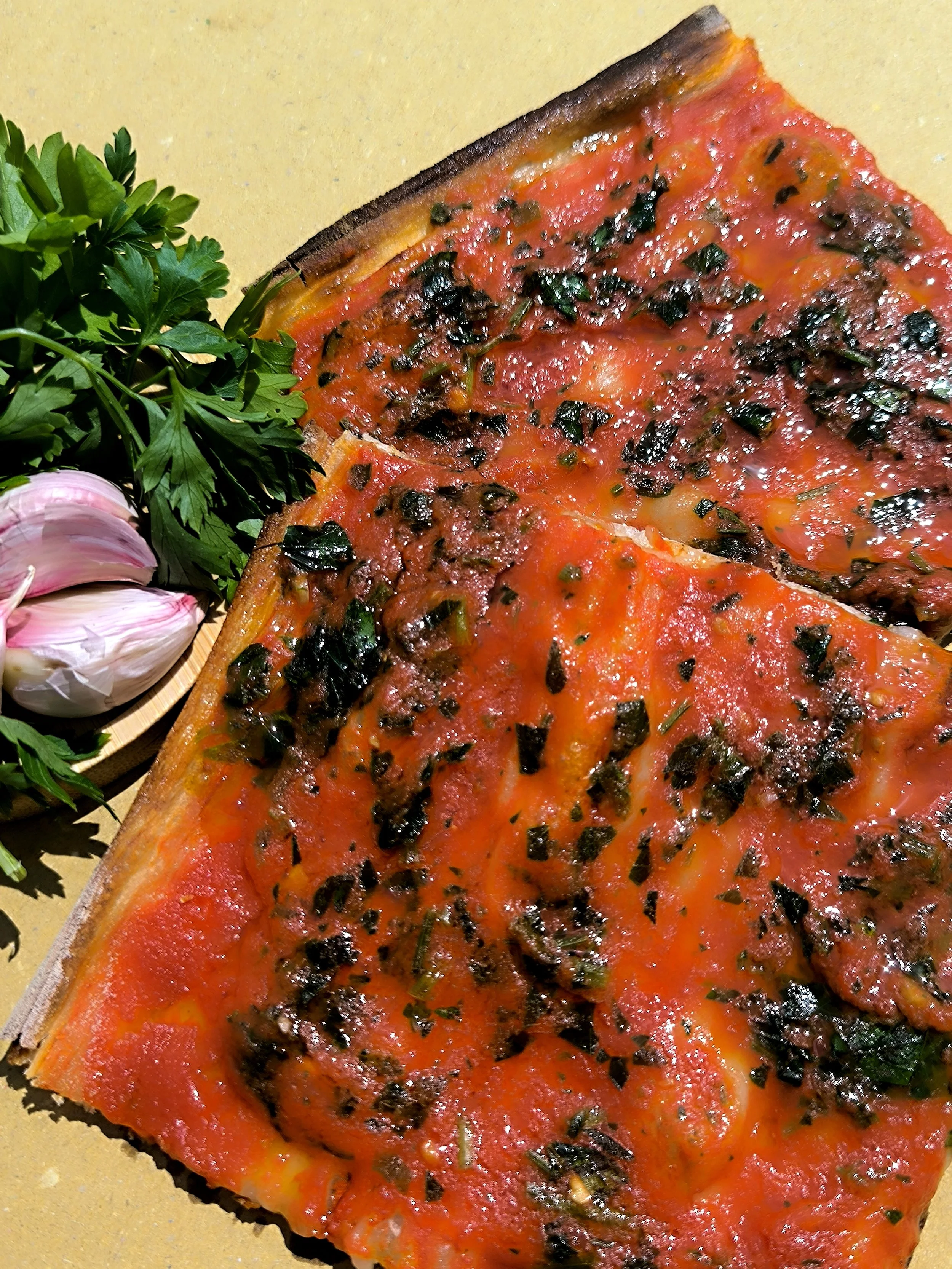 Una fetta di pizza margherita con pomodoro, basilico e formaggio, accompagnata da aglio, prezzemolo e cipolla