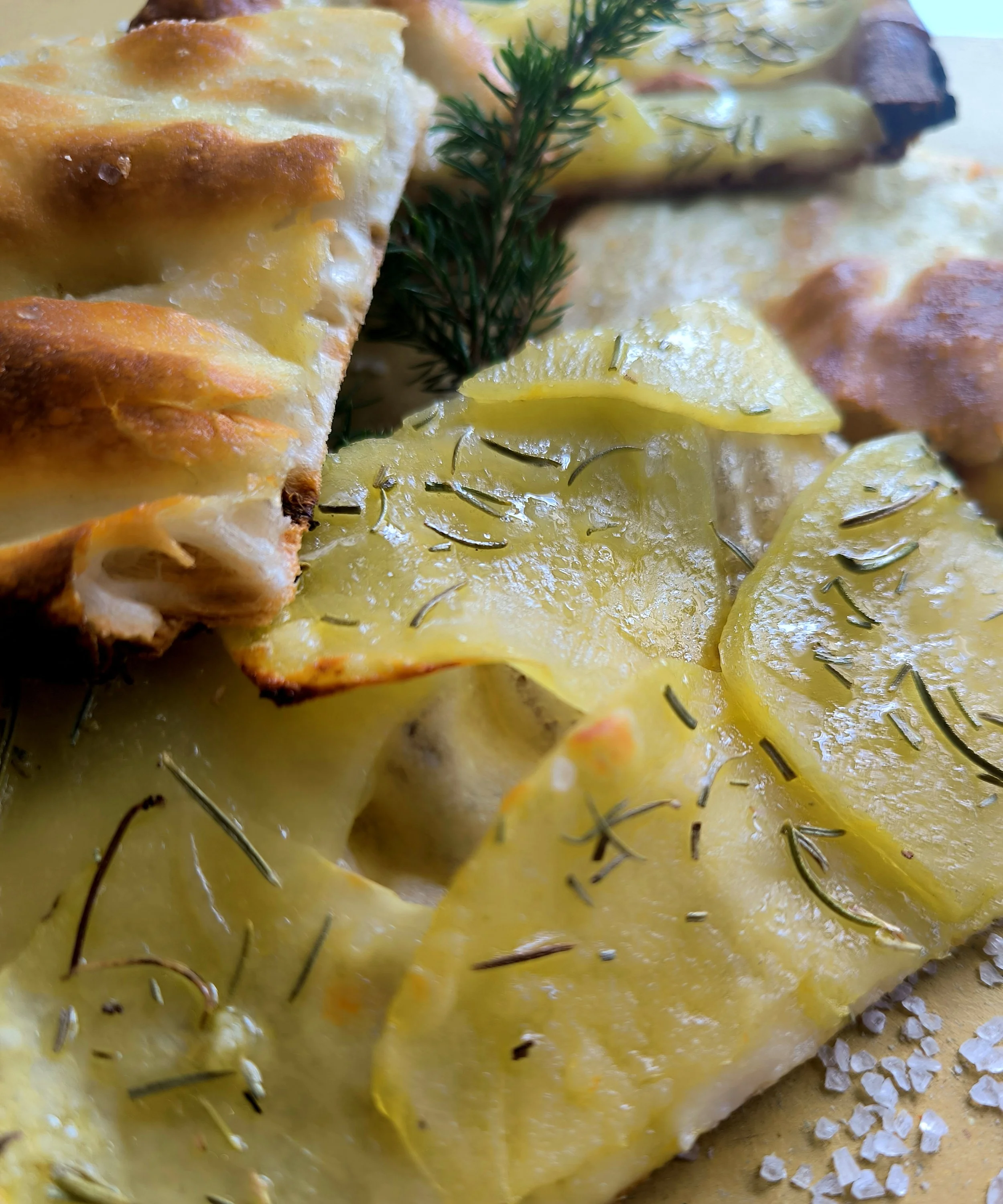 Fetta di quiche con patate, rosmarino e una foglia di prezzemolo, con sale grosso ai lati.