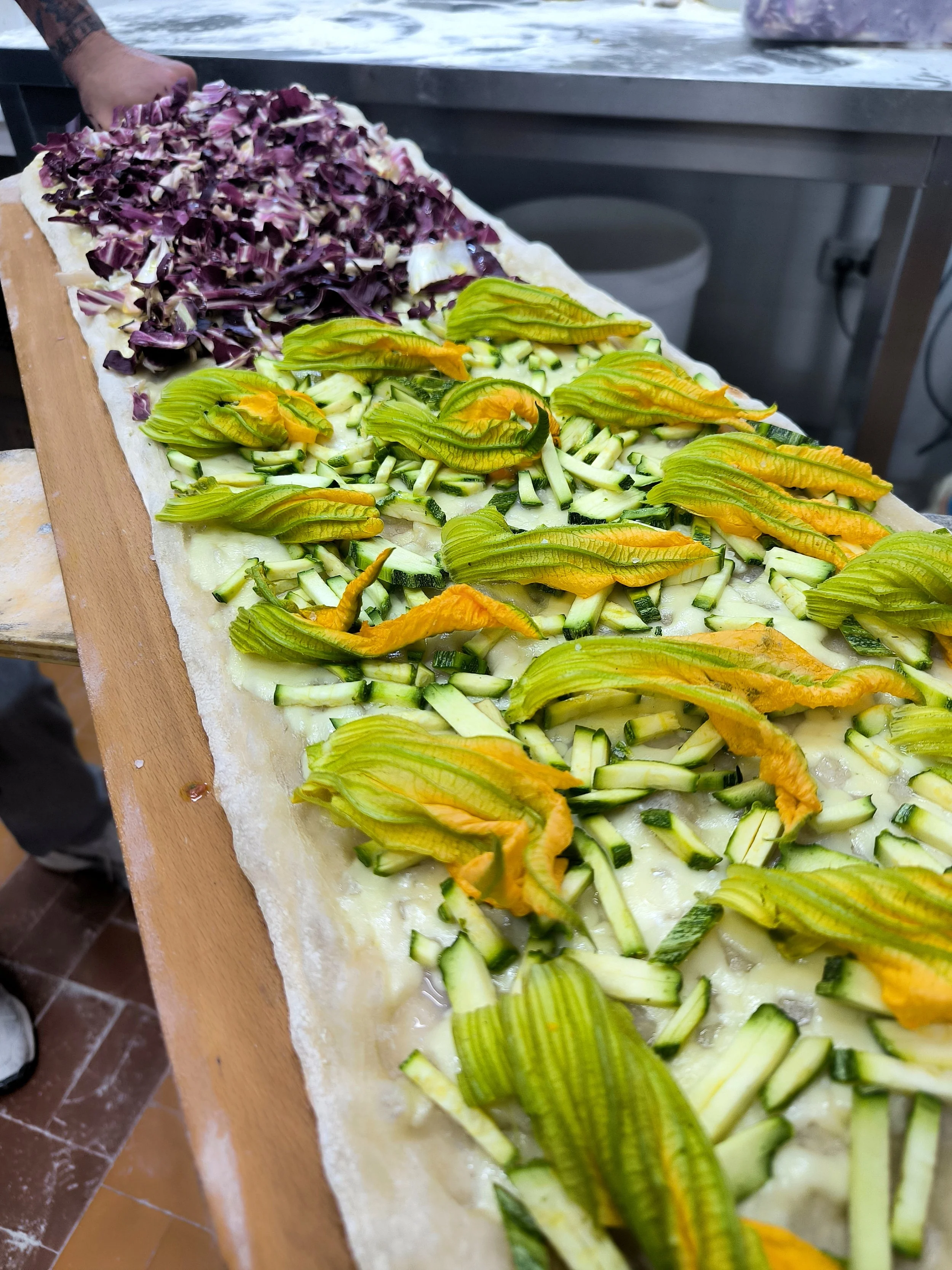 Preparazione di una pizza con verdure, con radicchio rosso, zucchine e melanzane su una tavola di legno.