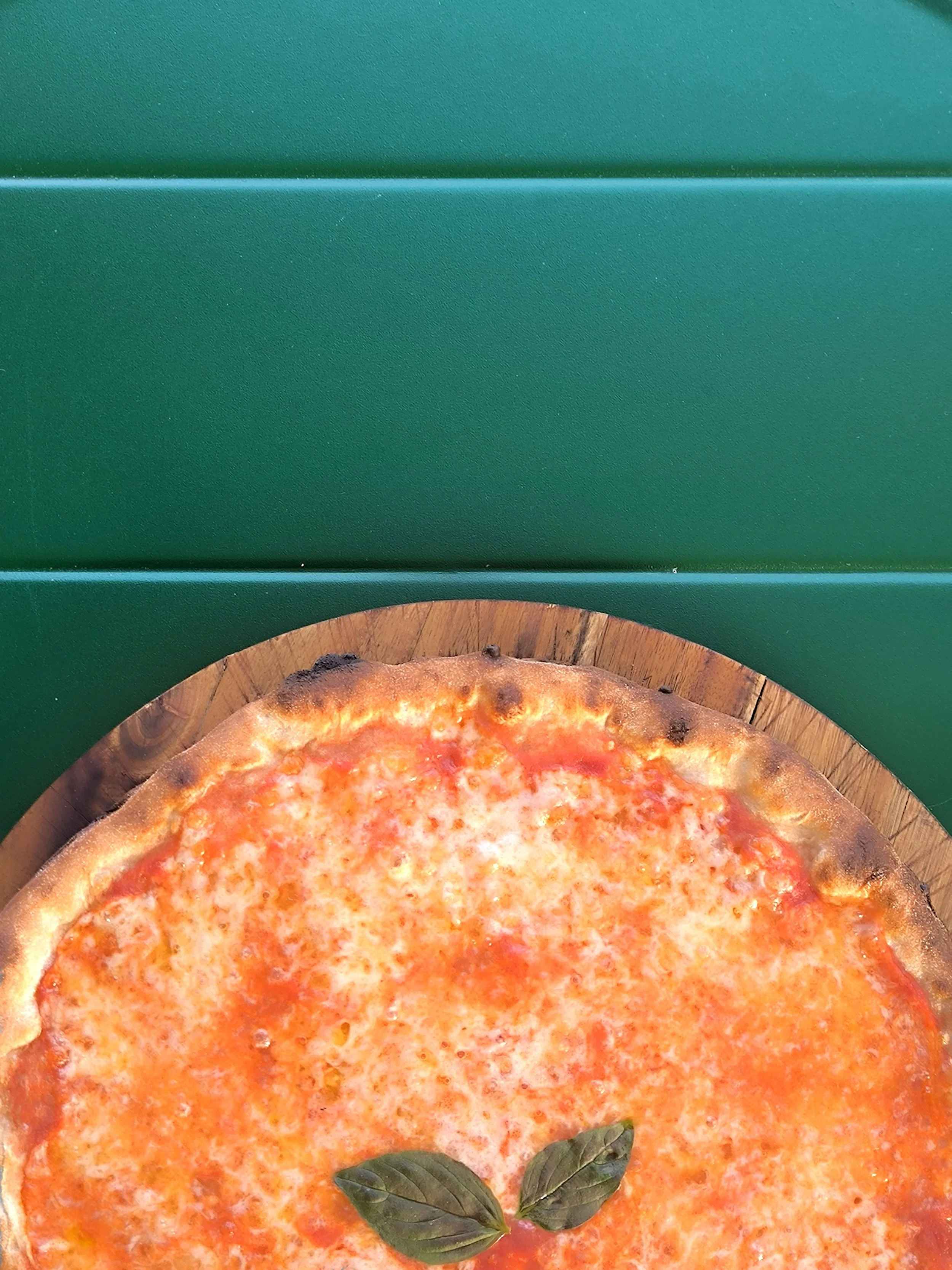 Pizza margherita con mozzarella e basilico fresco su un piatto di legno, sfondo verde.