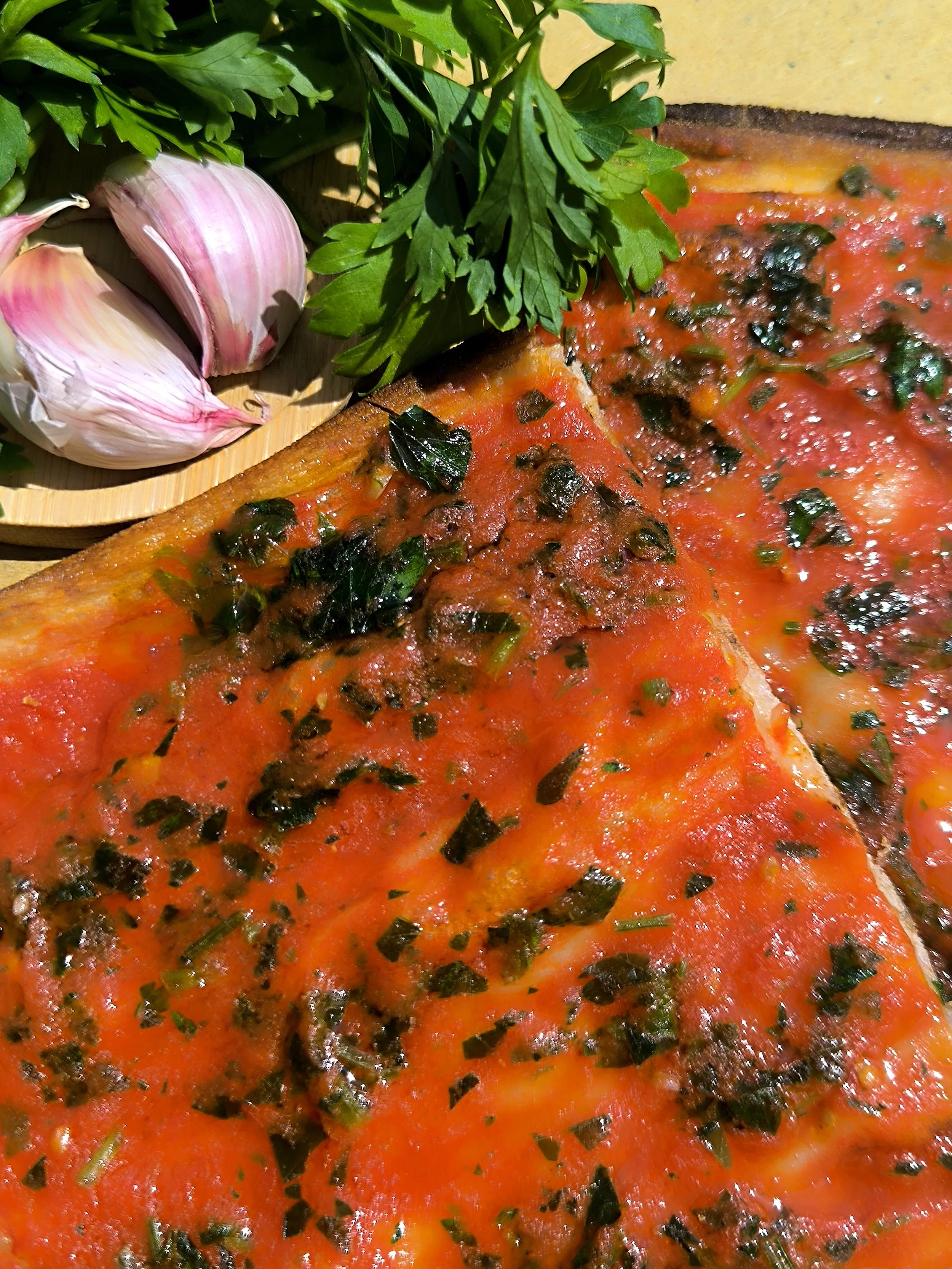 Piatto di pizza con salsa di pomodoro, basilico e pepe nero, accompagnata da aglio e prezzemolo.