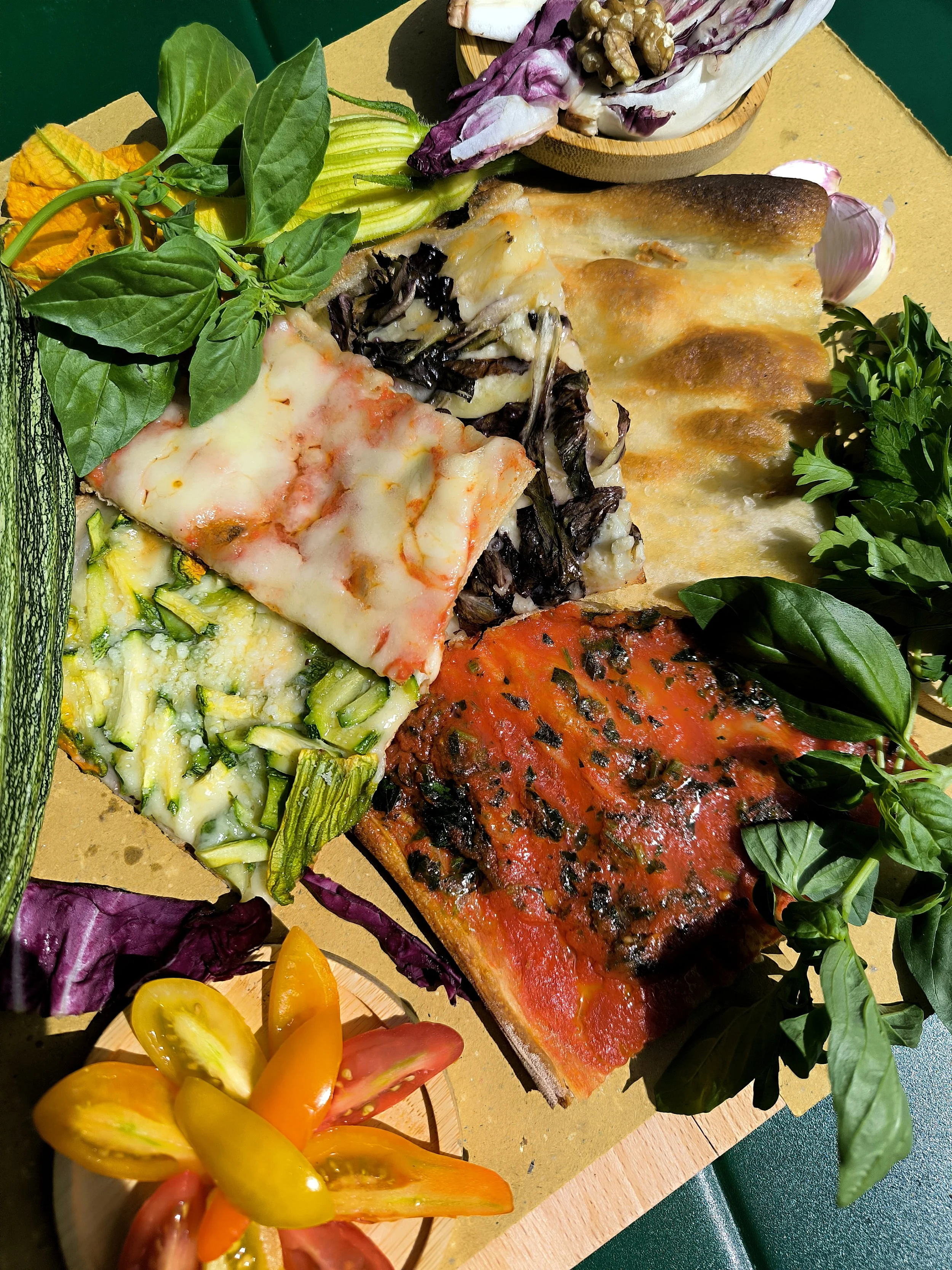 Porzione di pizza condita con pomodoro e basilico, accompagnata da insalate di verdure, pomodorini e foglie di basilico e menta.