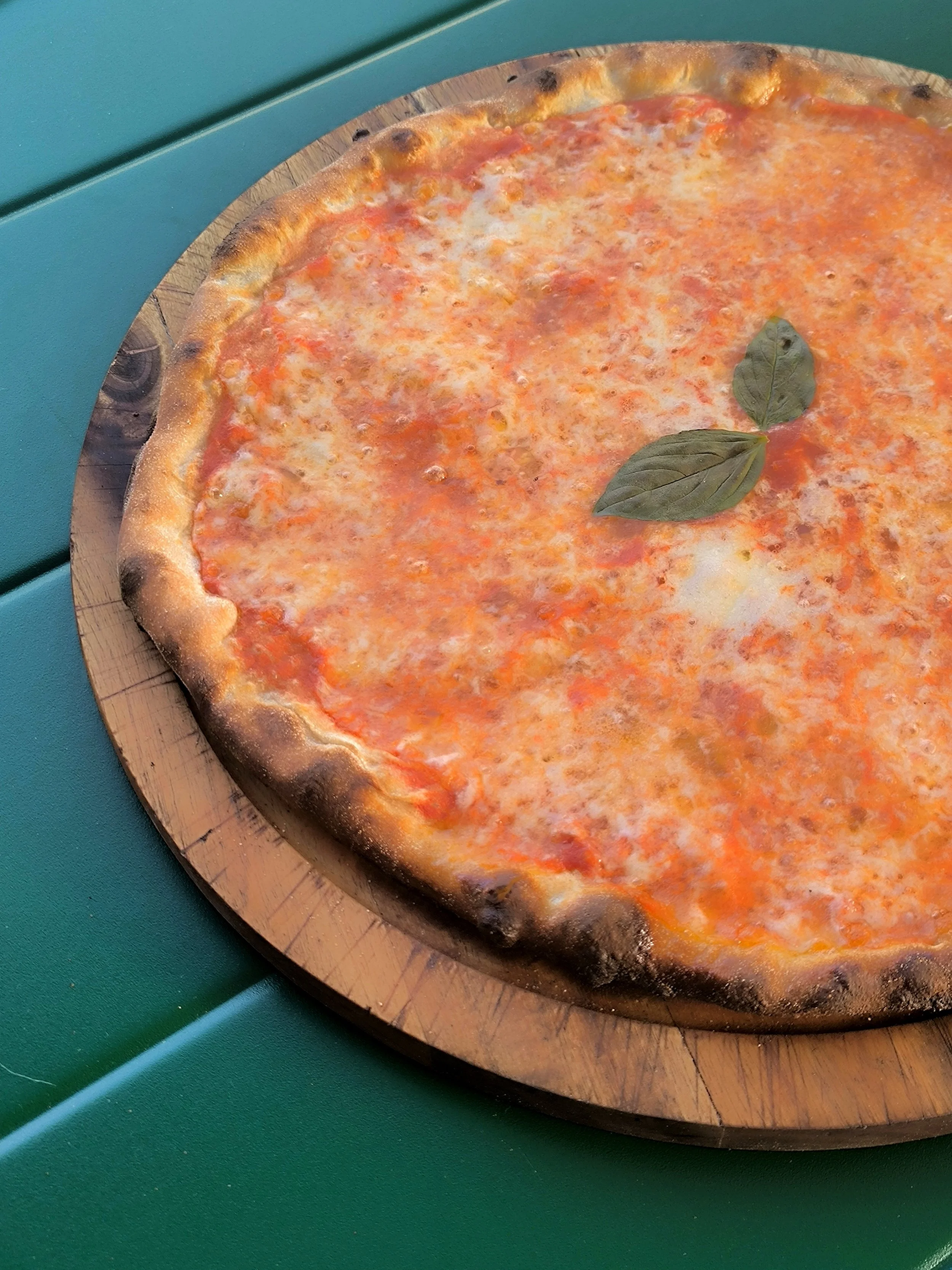 Una pizza margherita con pomodoro, mozzarella e foglie di basilico, posta su un tagliere di legno sopra una superficie verde.