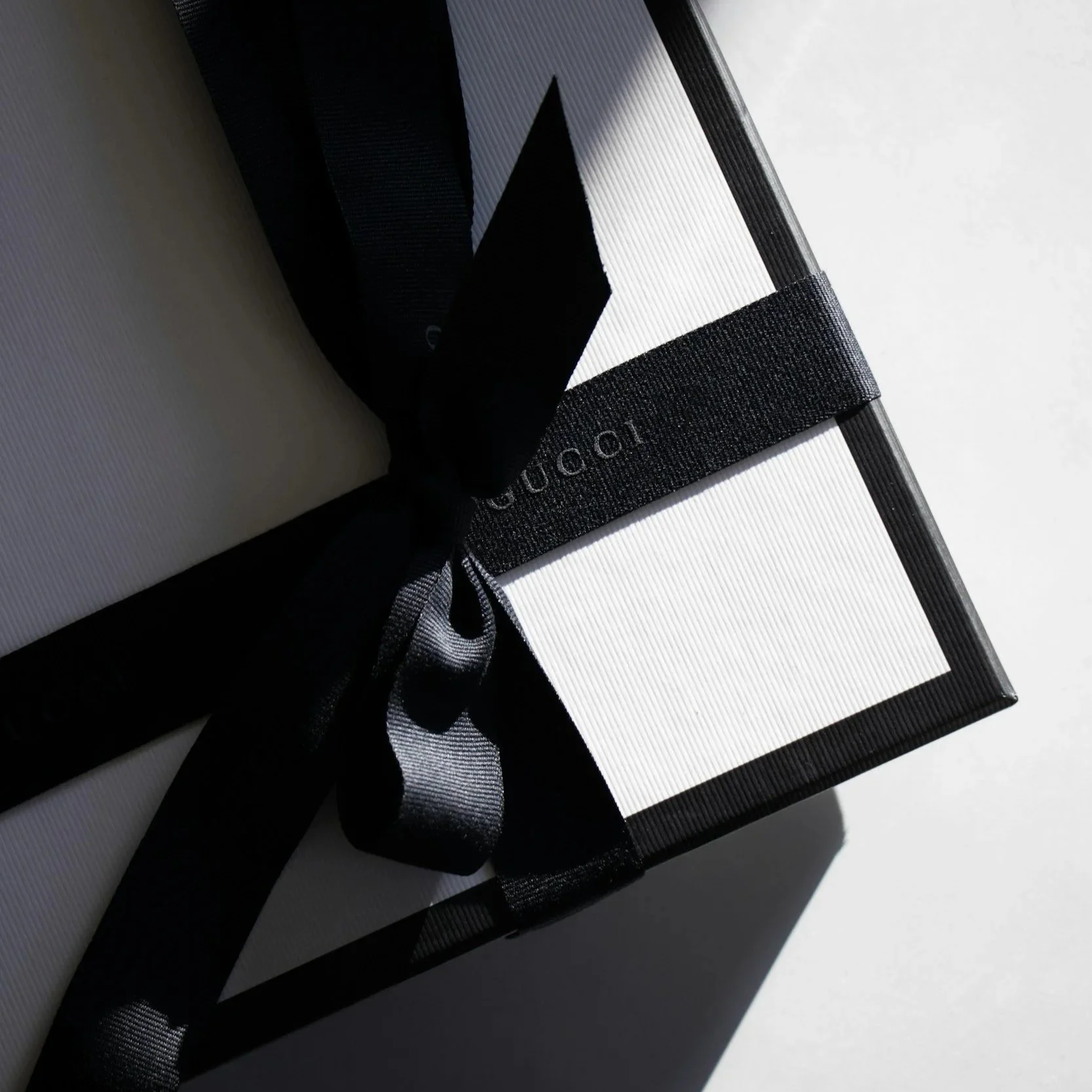 Close-up photo of a black and white book with a black ribbon bookmark, placed on a white surface and casting shadows.