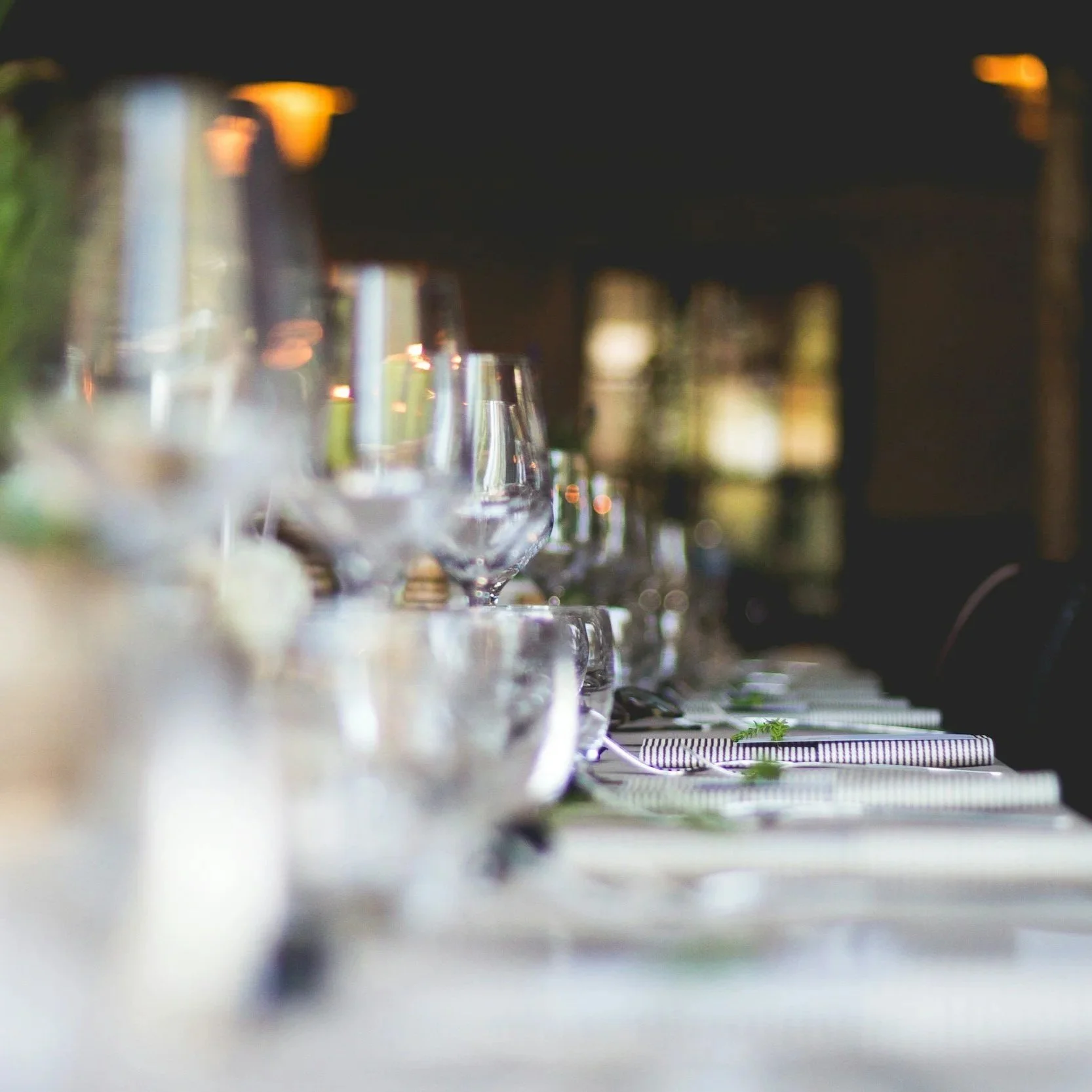 Close-up of an elegant table setup with wine glasses, cutlery, and a striped napkin, with a blurred background, possibly at a restaurant or dining event.
