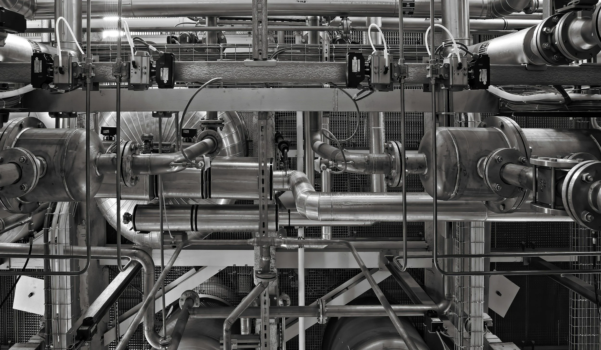 Industrial machinery with interconnected stainless steel pipes and valves, part of a factory or processing plant.