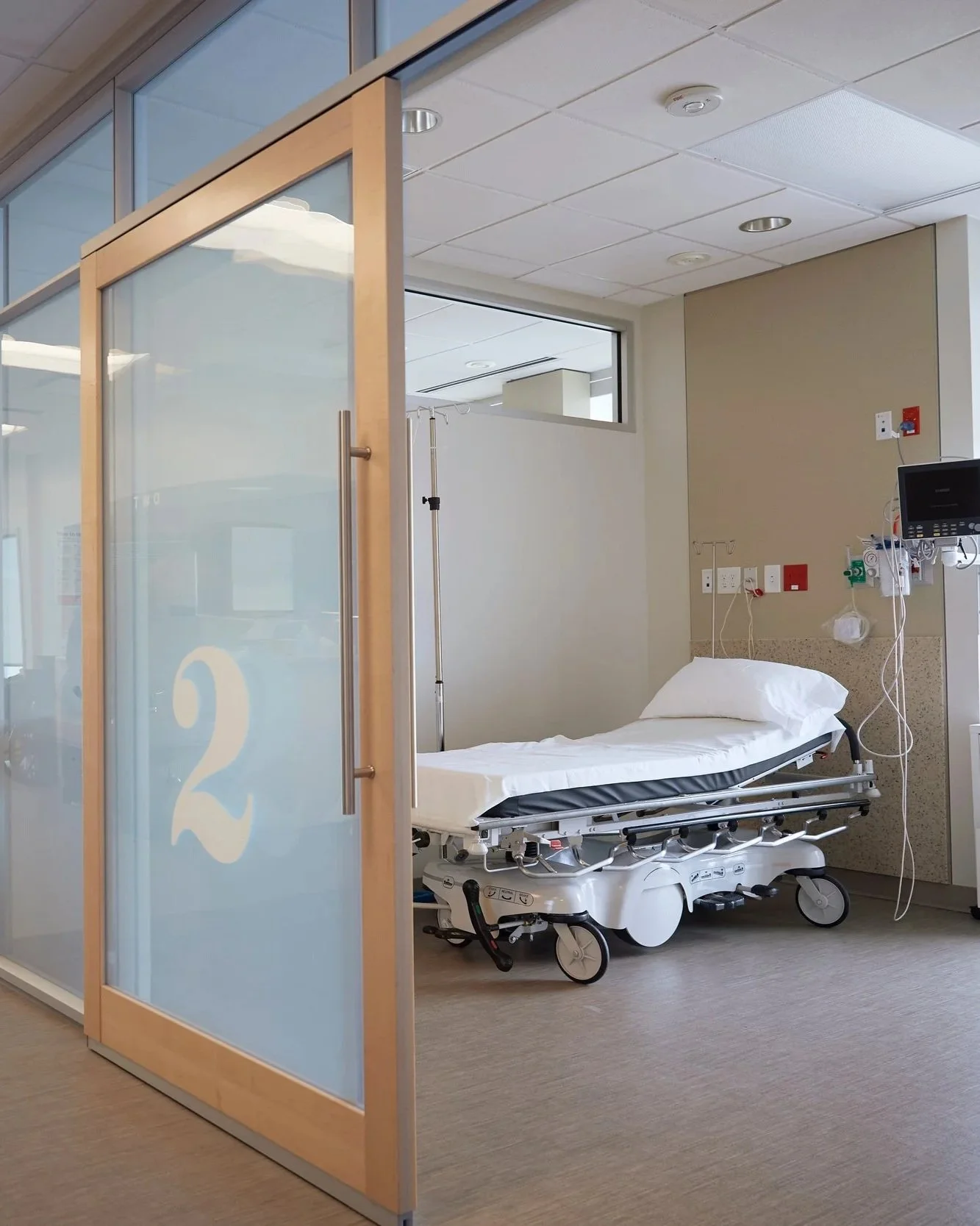 Empty hospital bed in a medical room with medical equipment and a privacy glass door.