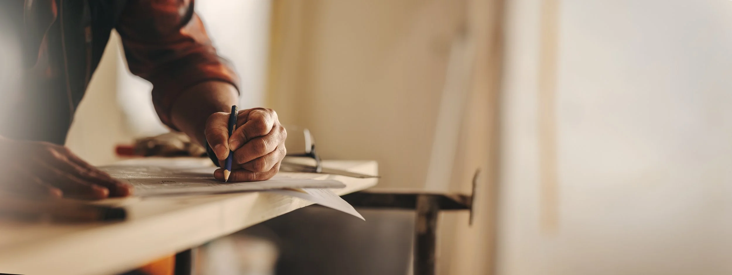 Close-up of a person writing with a blue pencil on a piece of paper on a table, with a neutral background.