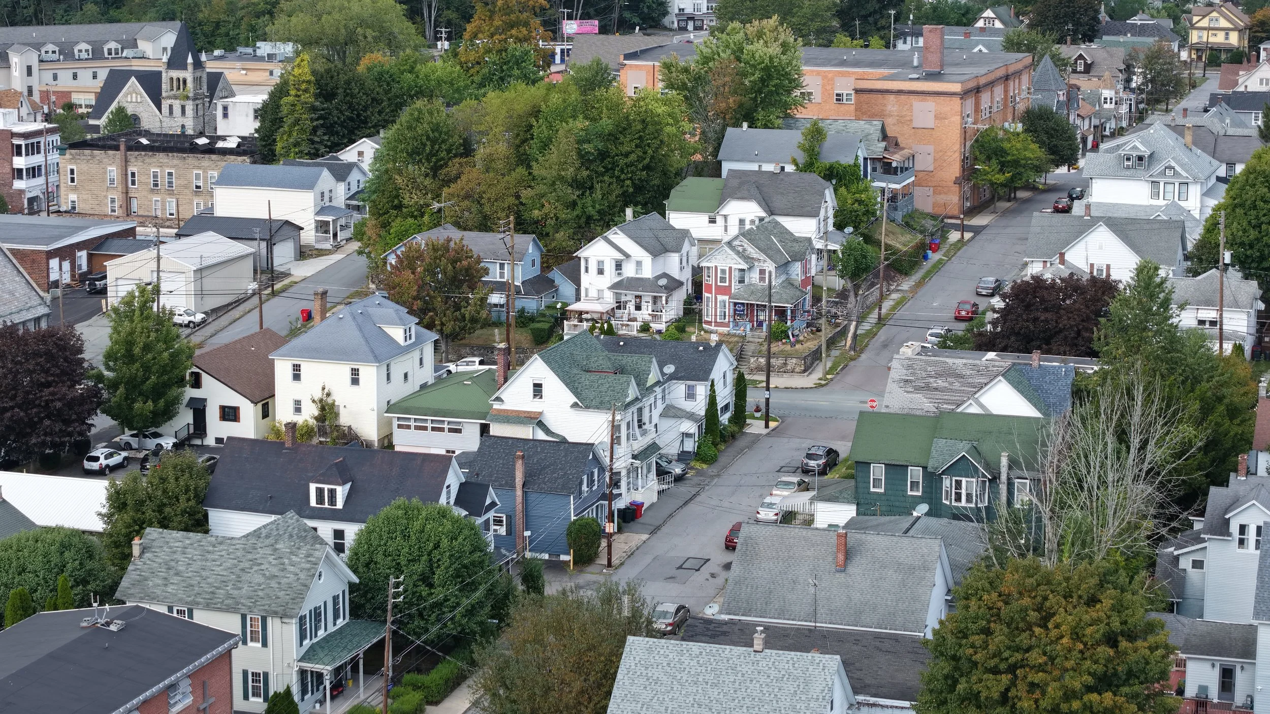 Aerial view of a residential neighborhood with various houses, trees, and parked cars on the streets.