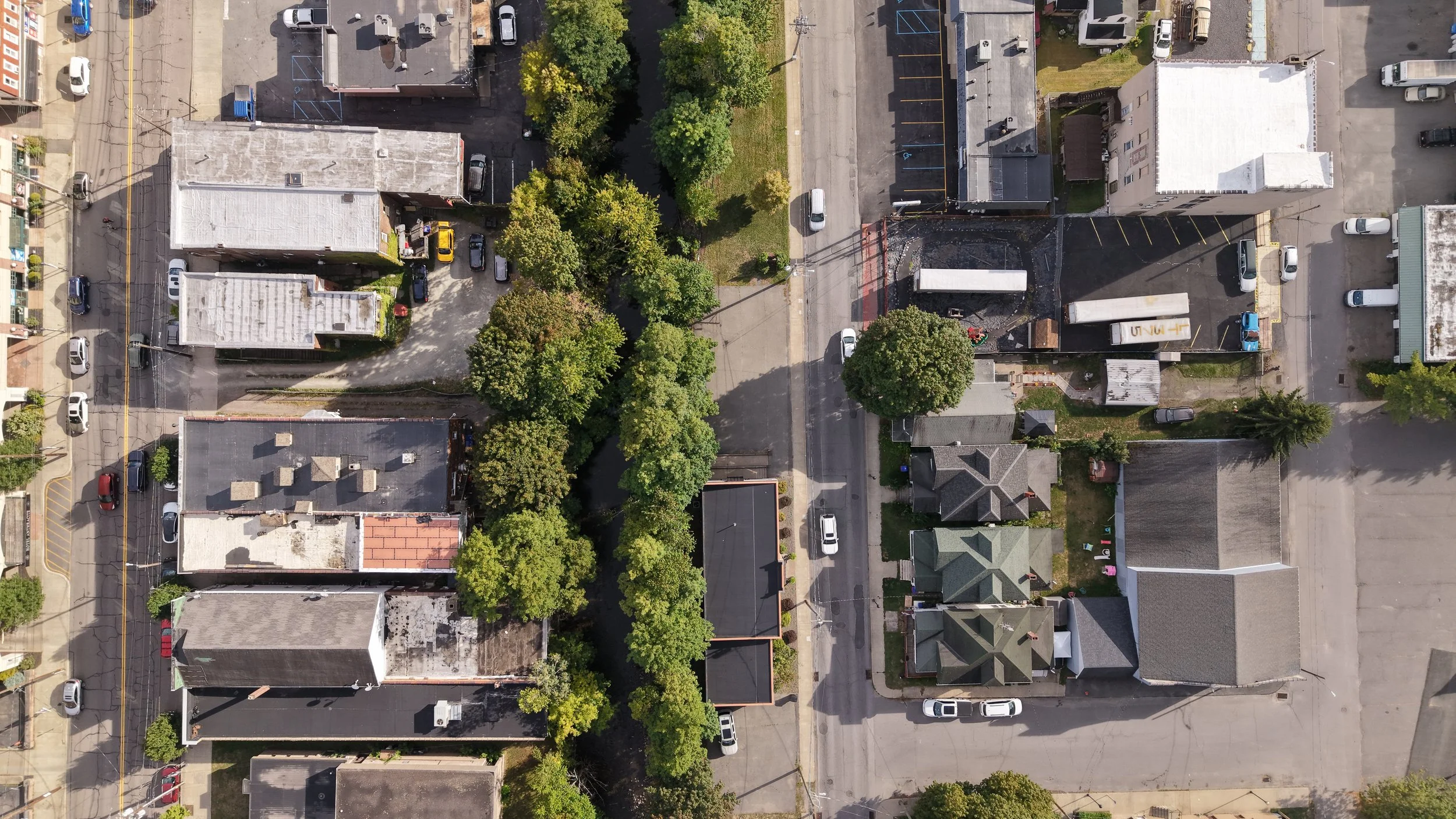 An aerial view of a small urban area with scattered residential buildings, parking lots, and trees.