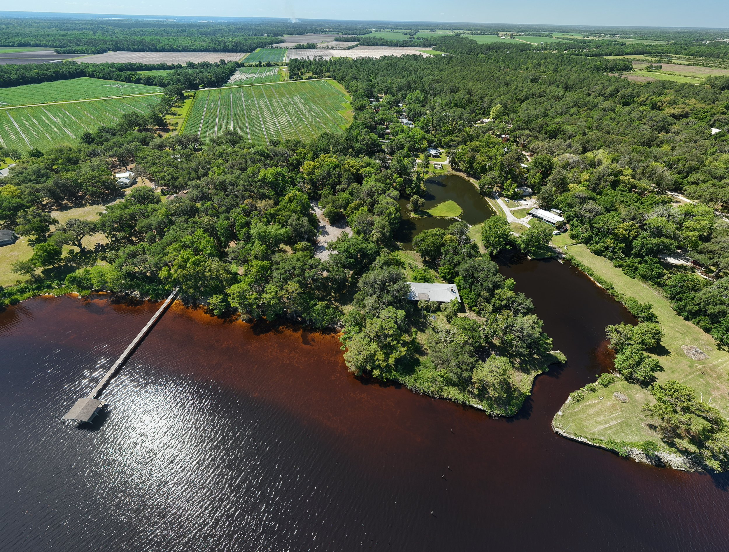An aerial view of a rural landscape with a river, dense trees, farmland, and a small community with houses and roads.