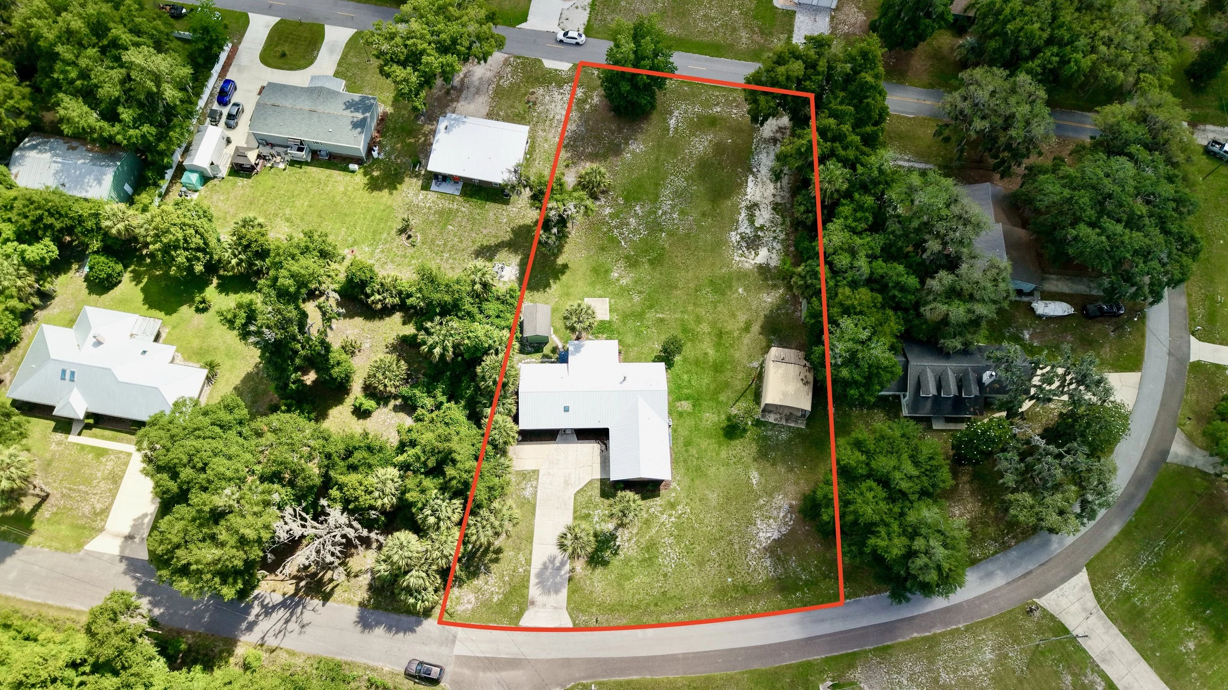 Aerial view of a residential neighborhood with a vacant lot outlined in red surrounded by trees and houses.