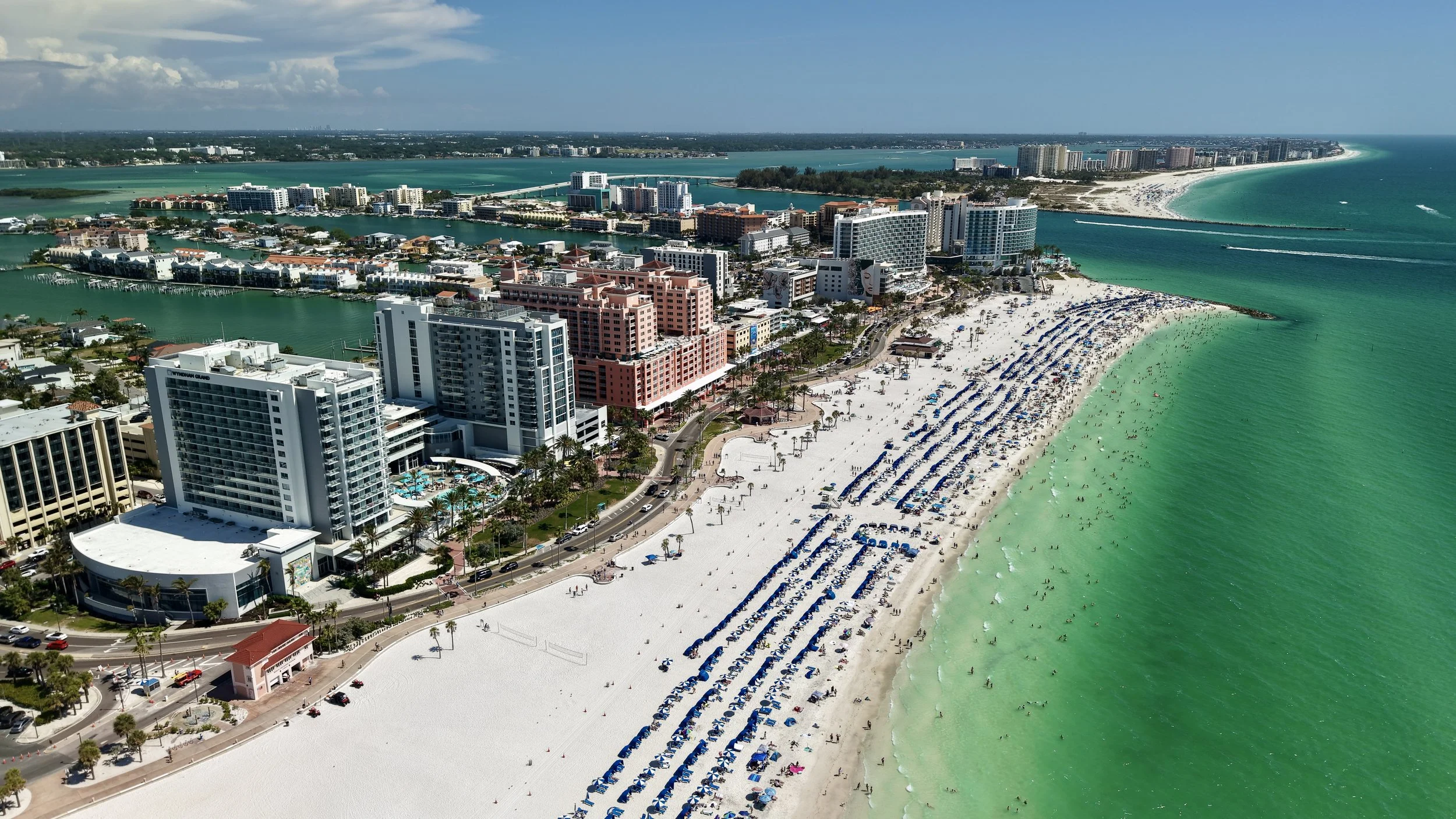 Aerial view of a beach and city skyline in Miami with white sandy beaches, turquoise water, high-rise buildings, and umbrellas on the beach.