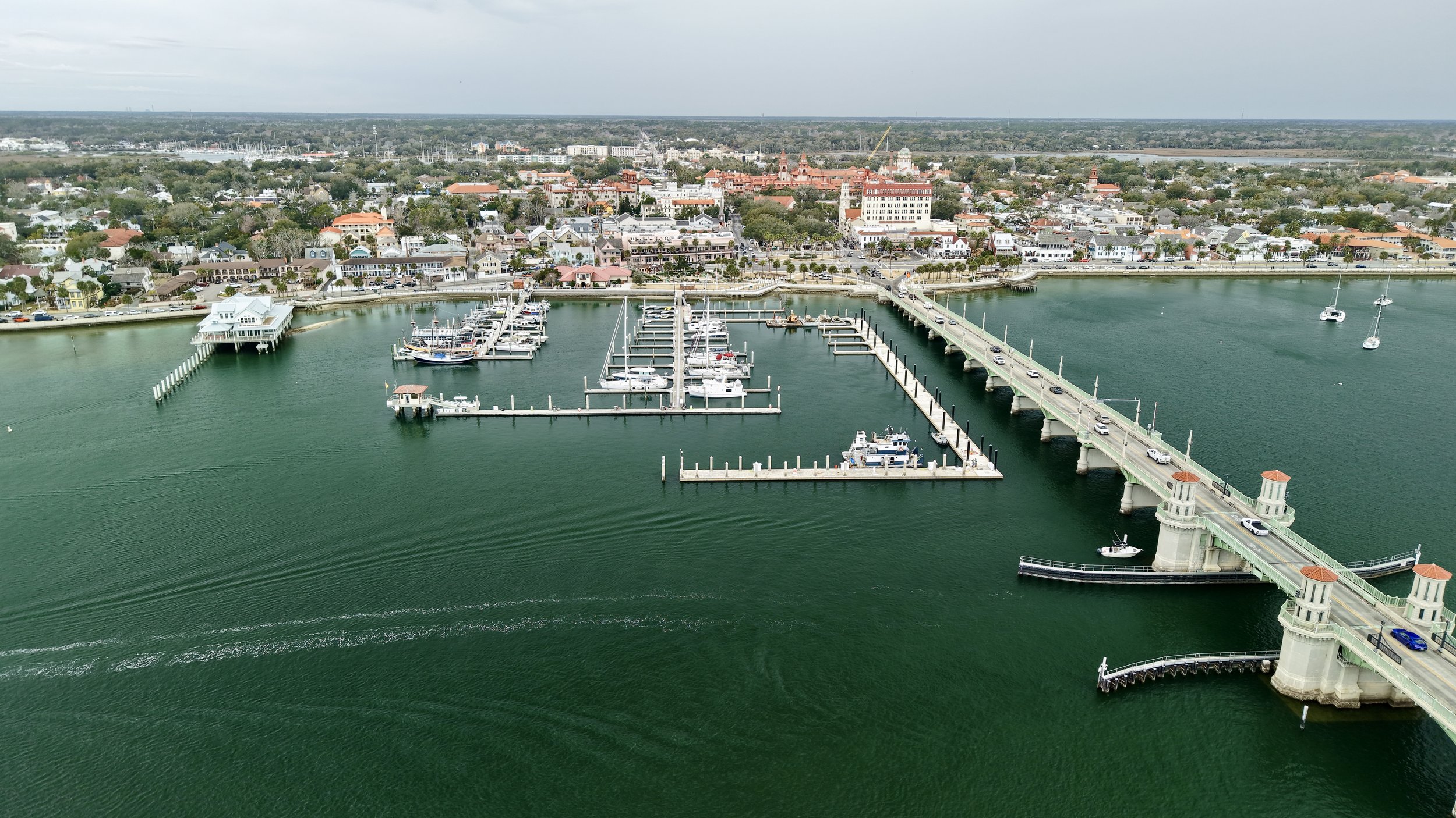 Aerial view of a marina with boats docked, a bridge connecting the city, and a historic town with colorful buildings and waterfront.
