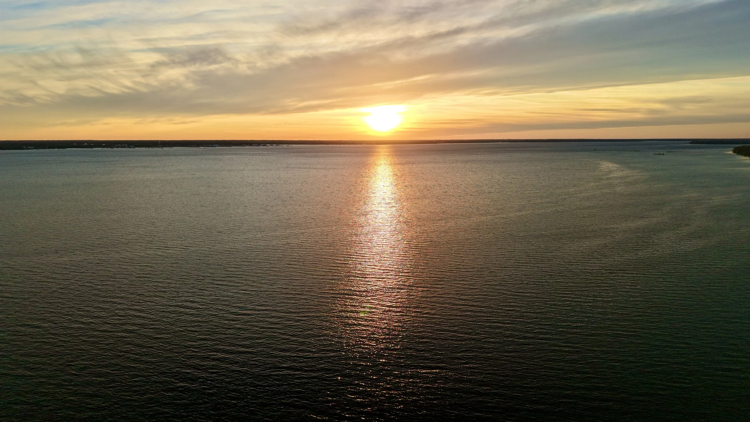 Sunset over a large body of water with clouds in the sky.