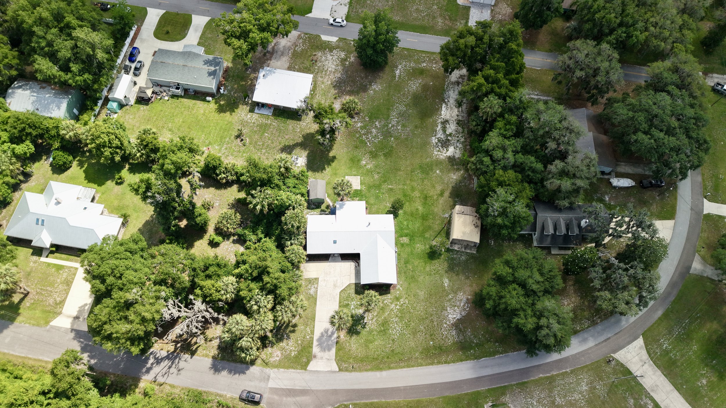 Aerial view of a residential neighborhood with several houses, trees, lawns, and a curved street.