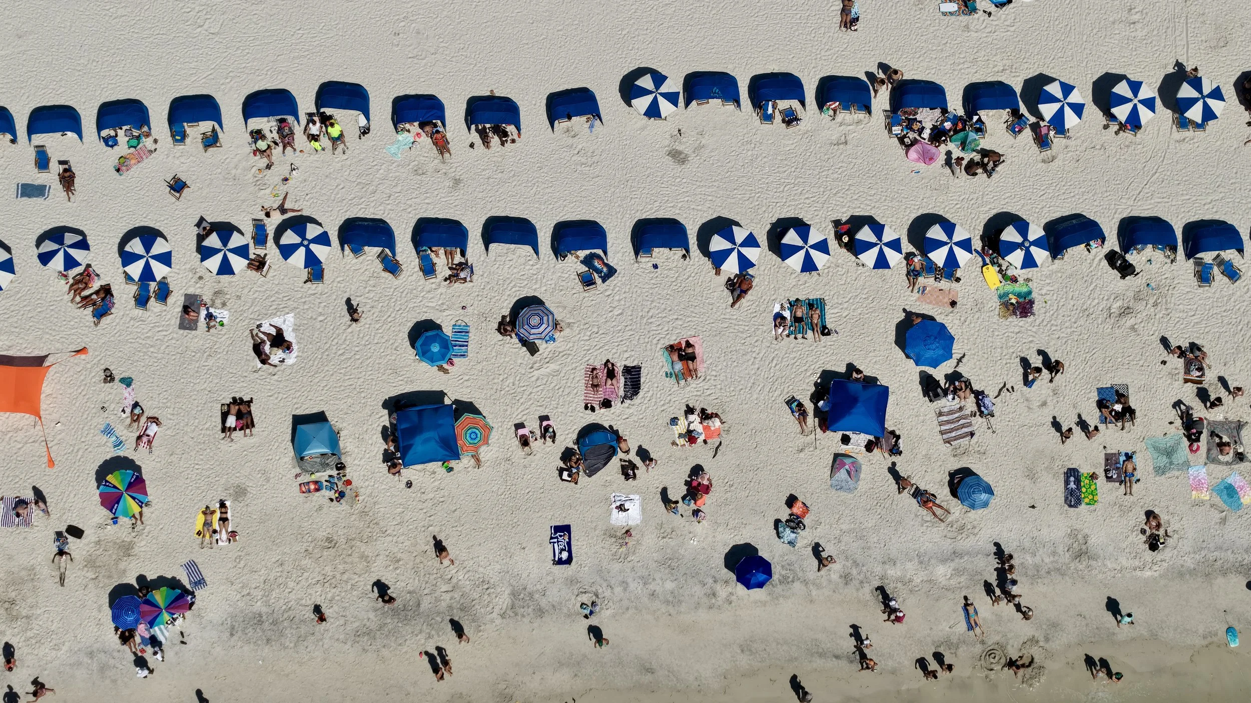 Aerial view of a crowded beach with many umbrellas, beach chairs, and people relaxing on the sand.