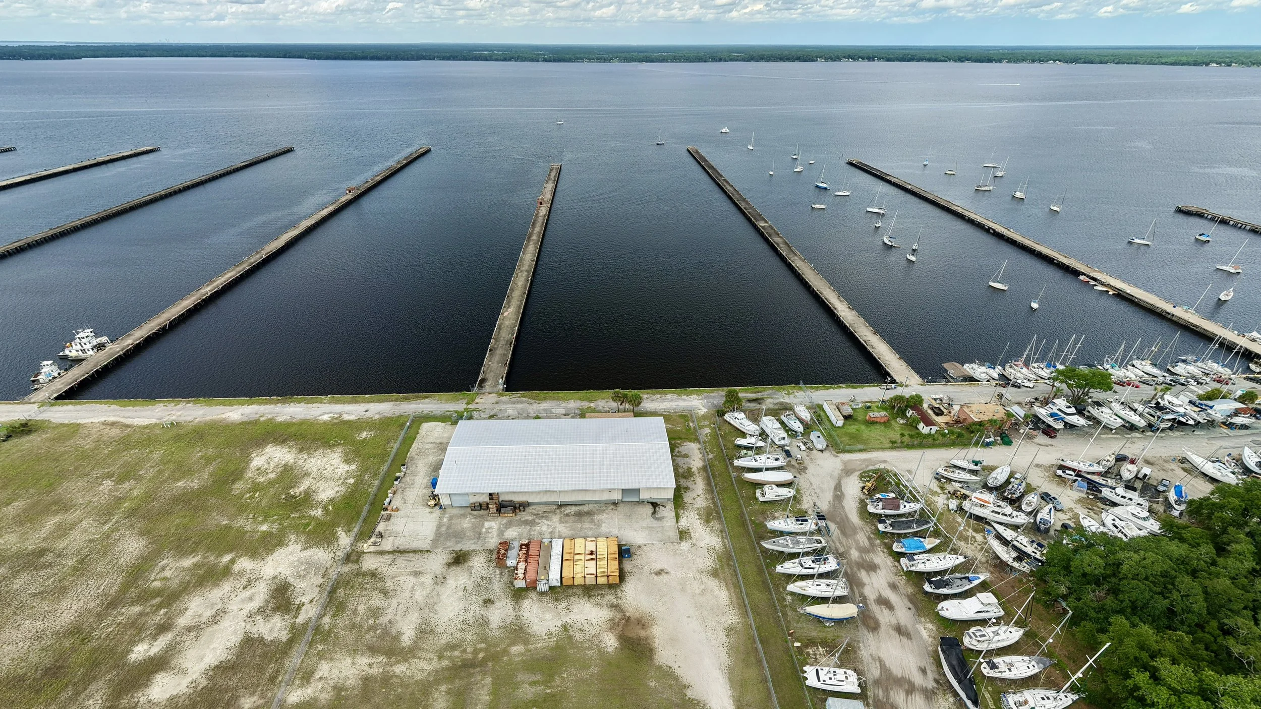 Aerial view of a marina with multiple boat docks, boats moored along the piers, and a parking lot with boats and trailers outside.
