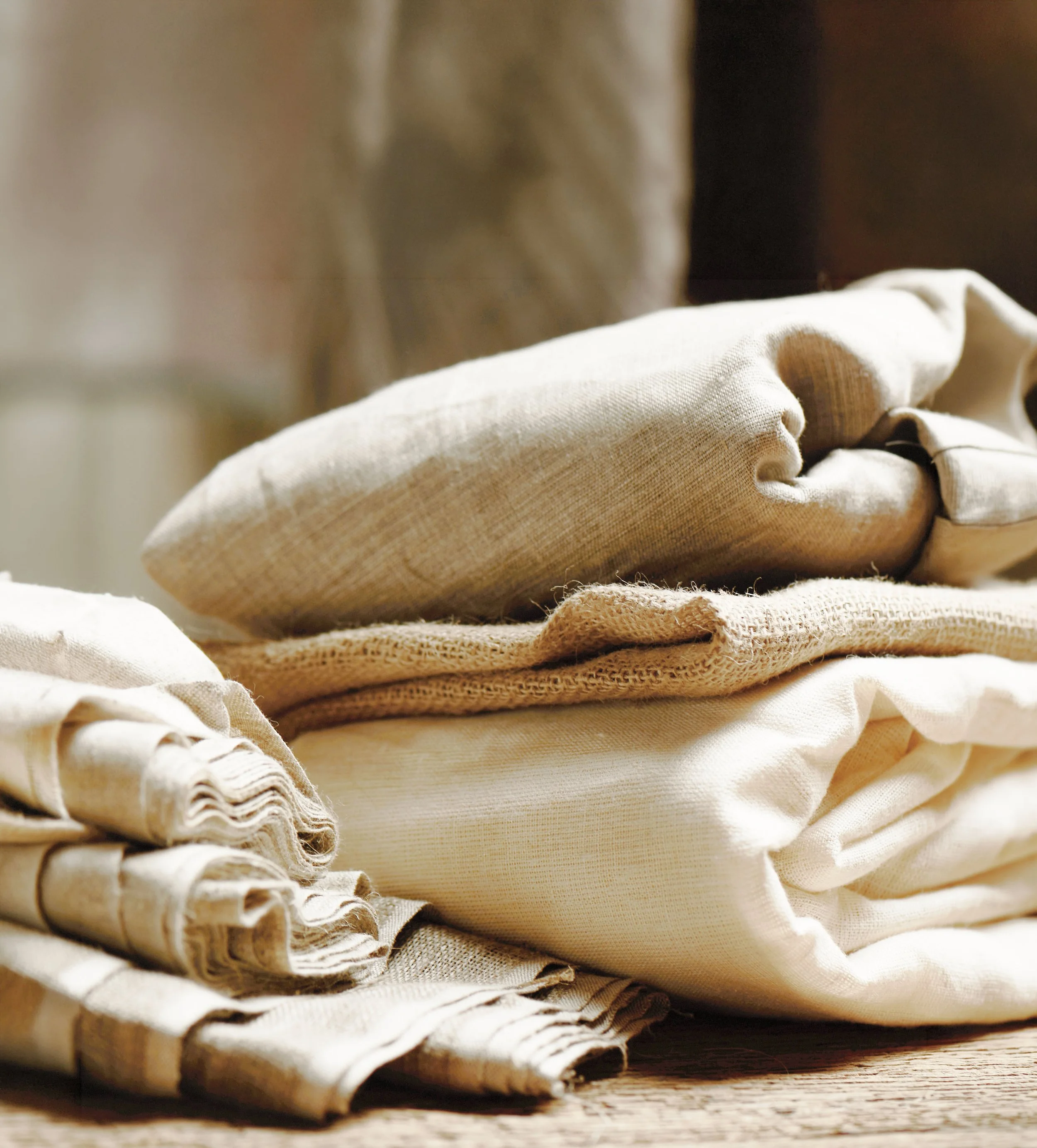 Stacked beige and neutral-colored fabric linens or towels on a wooden surface.