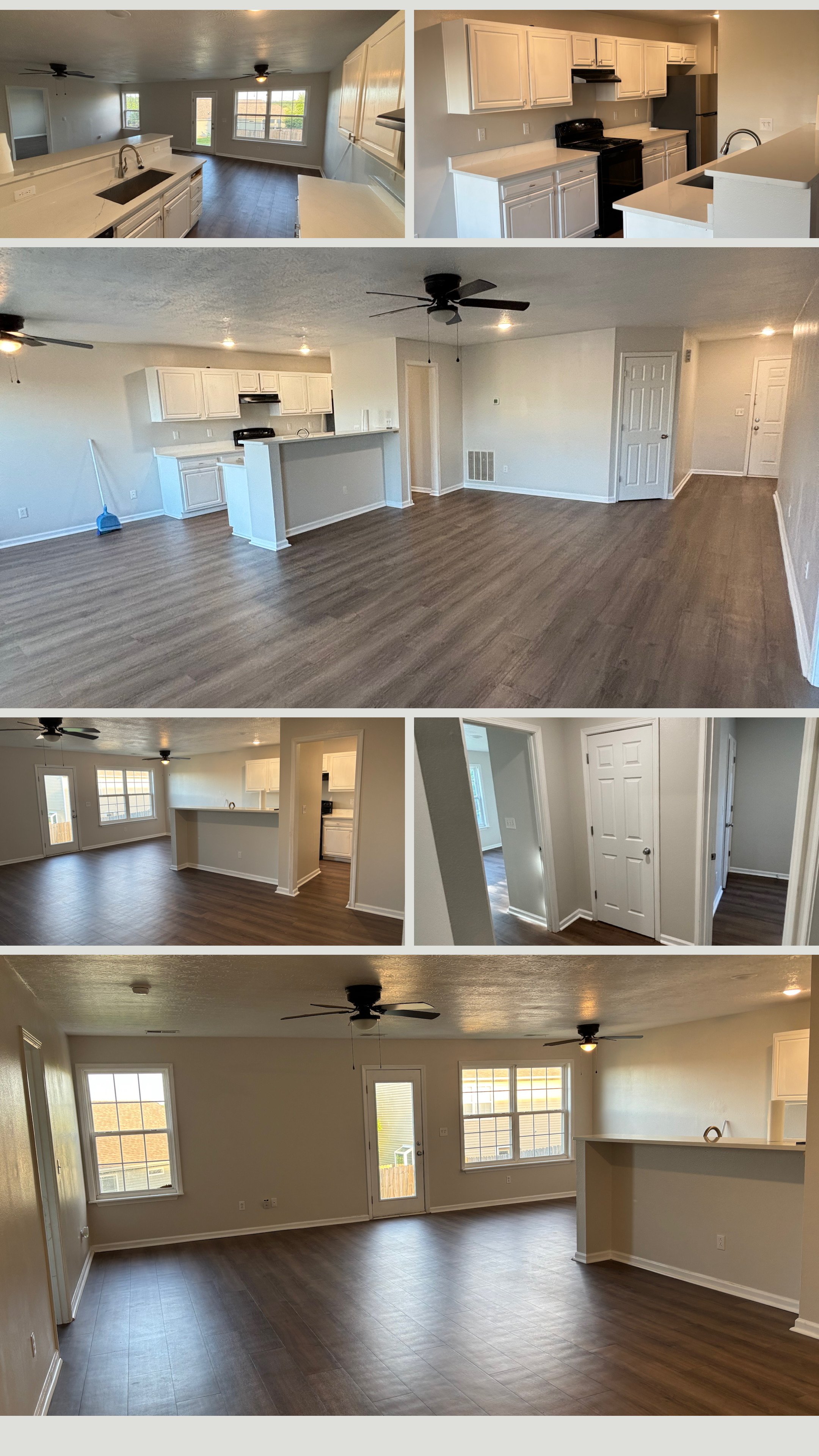 Open-plan living room and kitchen area with white cabinets, dark wood flooring, large windows, and ceiling fans, showing a modern, unfurnished interior.