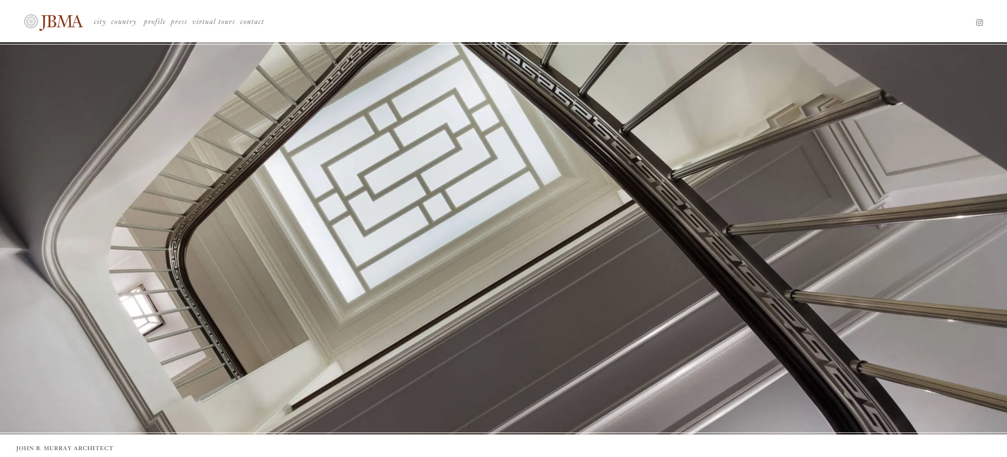 Interior view of a staircase looking up towards a ceiling skylight with geometric pattern, featuring ornate railings and decorative molding.