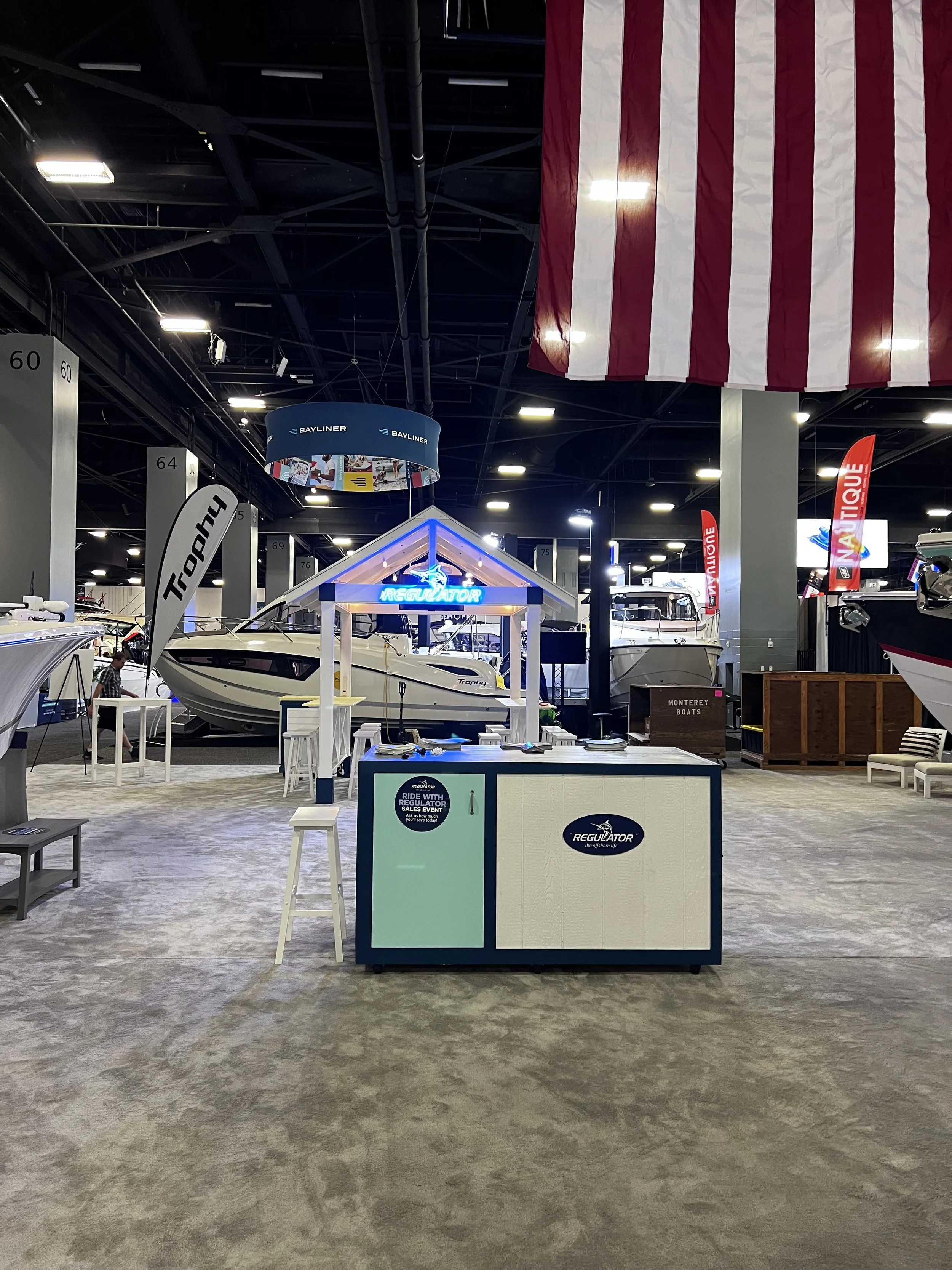 Indoor boat showroom with boats on display, a large flag hanging from the ceiling, and a registration desk in the foreground.