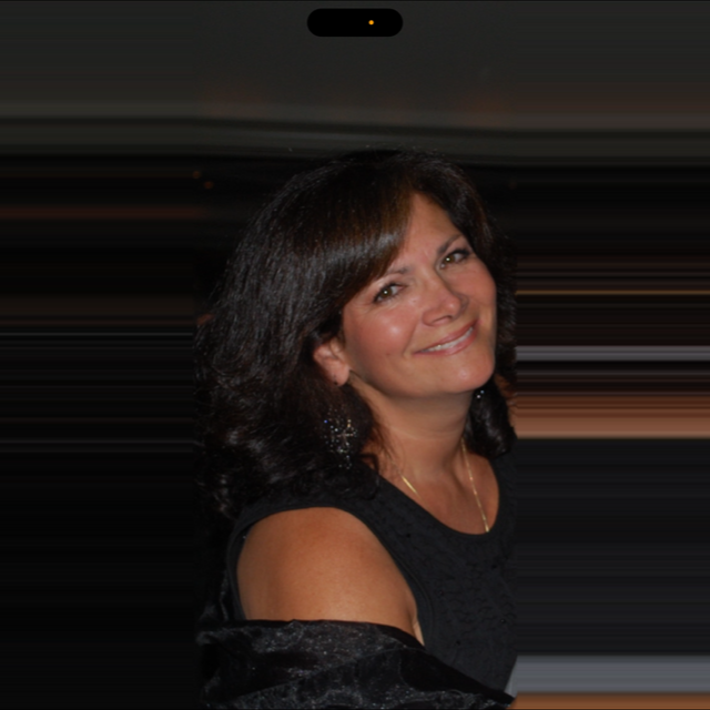 A woman with shoulder-length dark hair smiling at the camera, wearing a black sleeveless top and earrings, with a dark background and soft lighting.