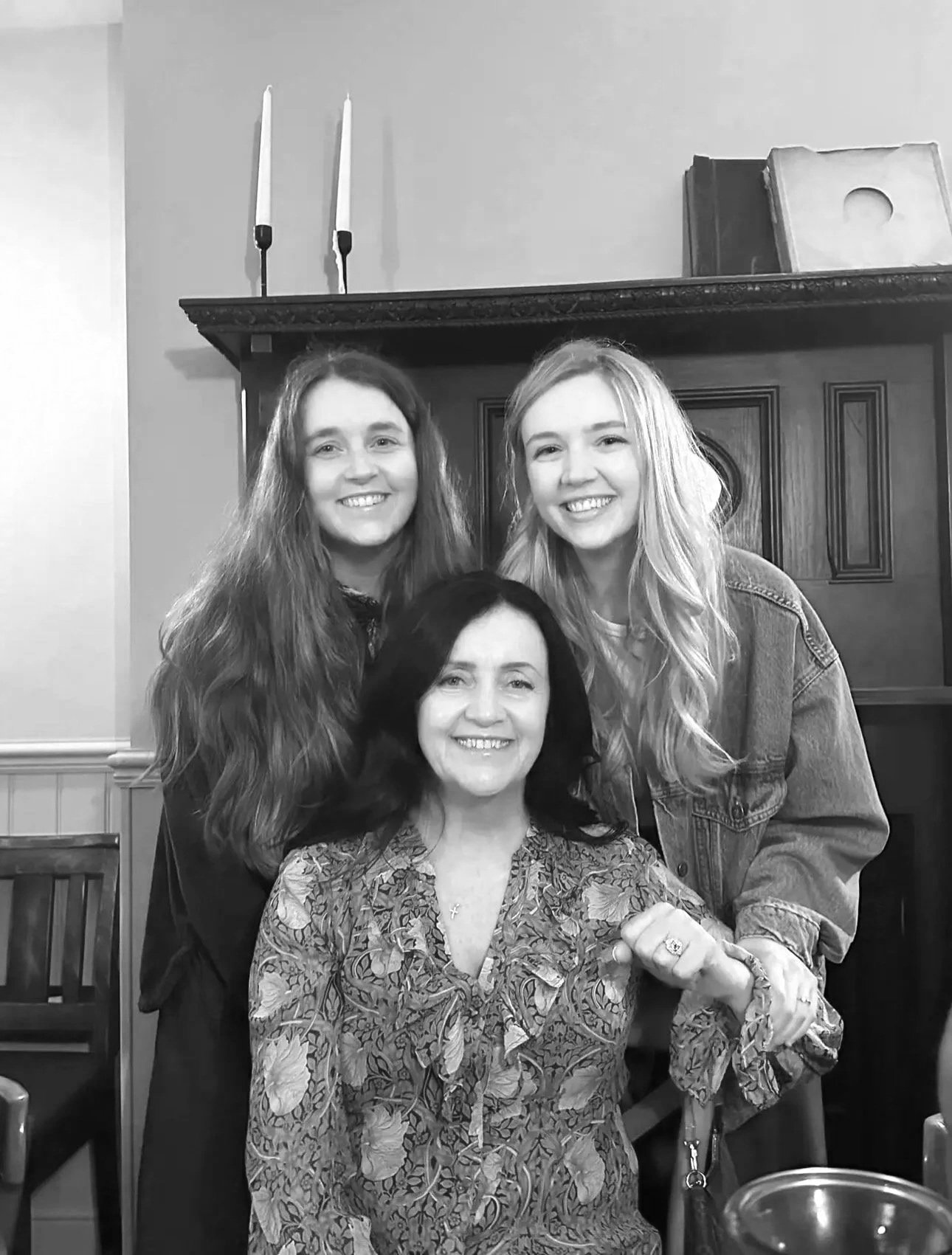 Black and white photo of three women smiling in a cozy, warmly decorated room. T