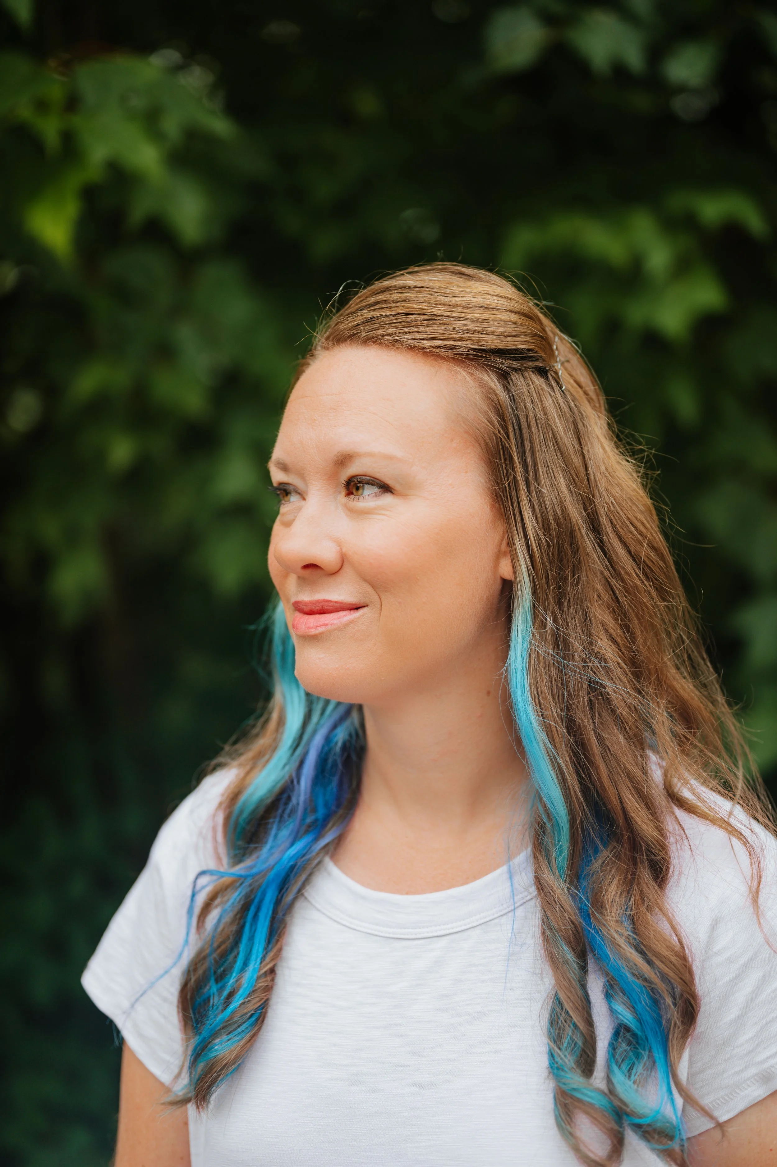 Image of a woman in profile with brown and blue hair with a slight smile and a green background