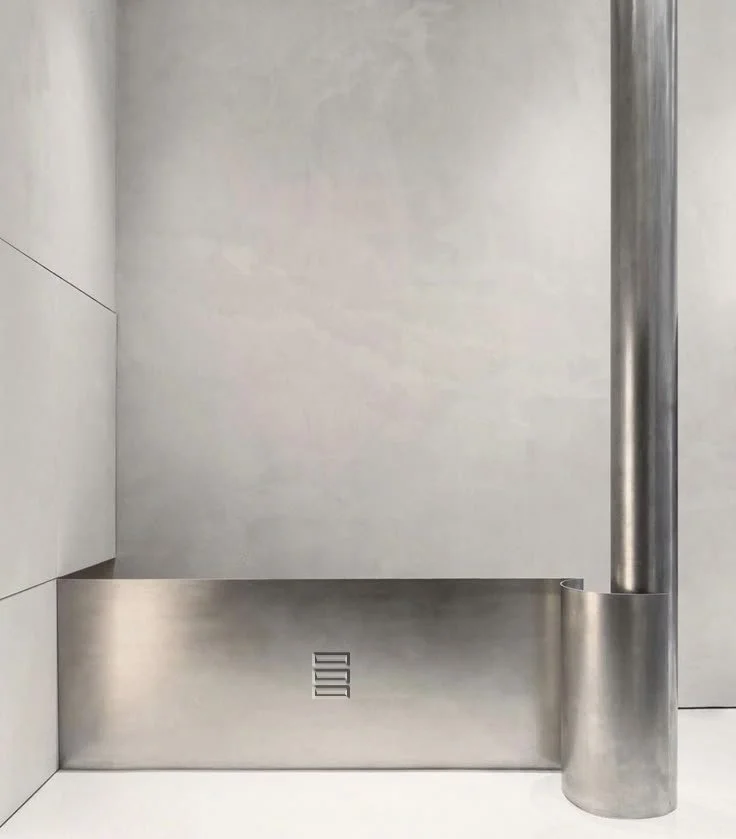 Minimalist modern interior with metal bench and cylindrical metal pole, gray wall background.