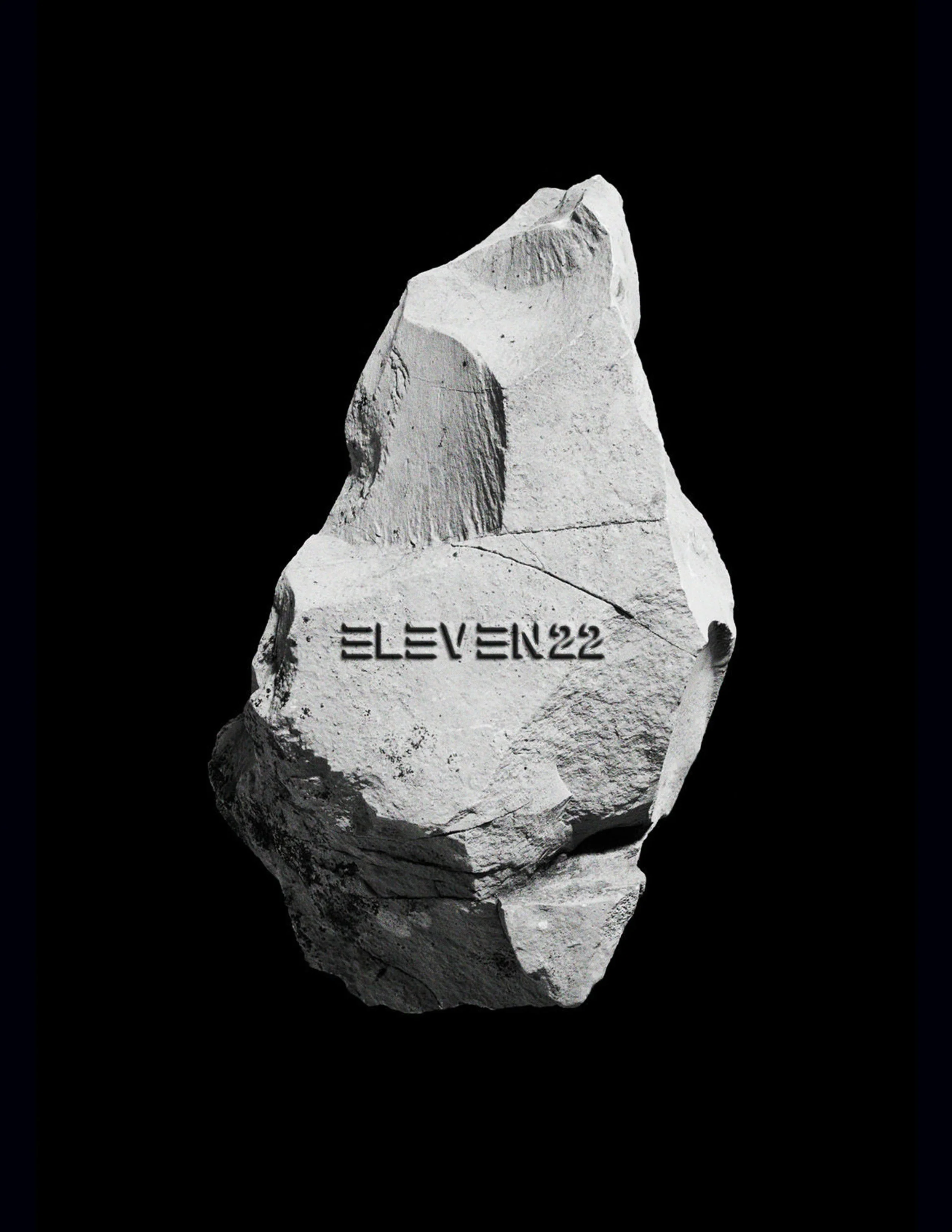 A large gray rock with the word 'ELEVEN22' engraved on it, set against a black background.