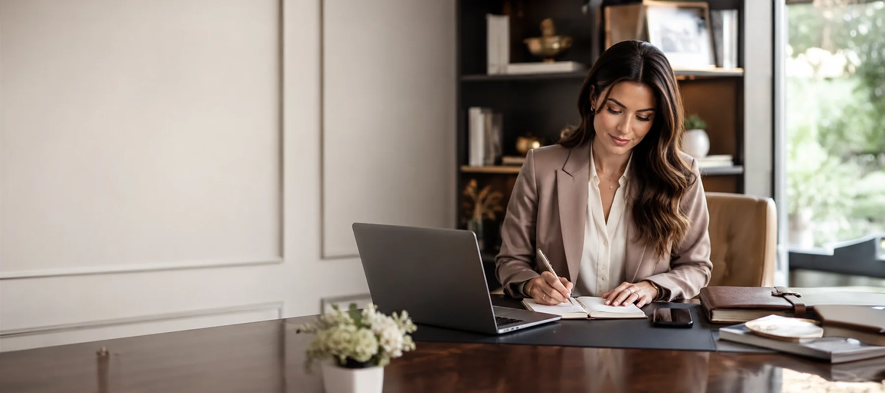 Female executive assistant writing notes at a laptop in an elegant private office, representing discreet high-level administrative support.