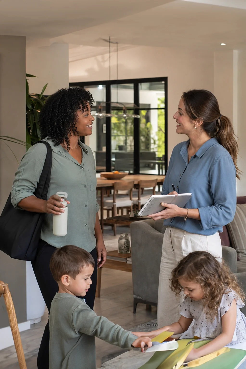 Two ROTA nannies coordinating childcare while children play in a modern family home.