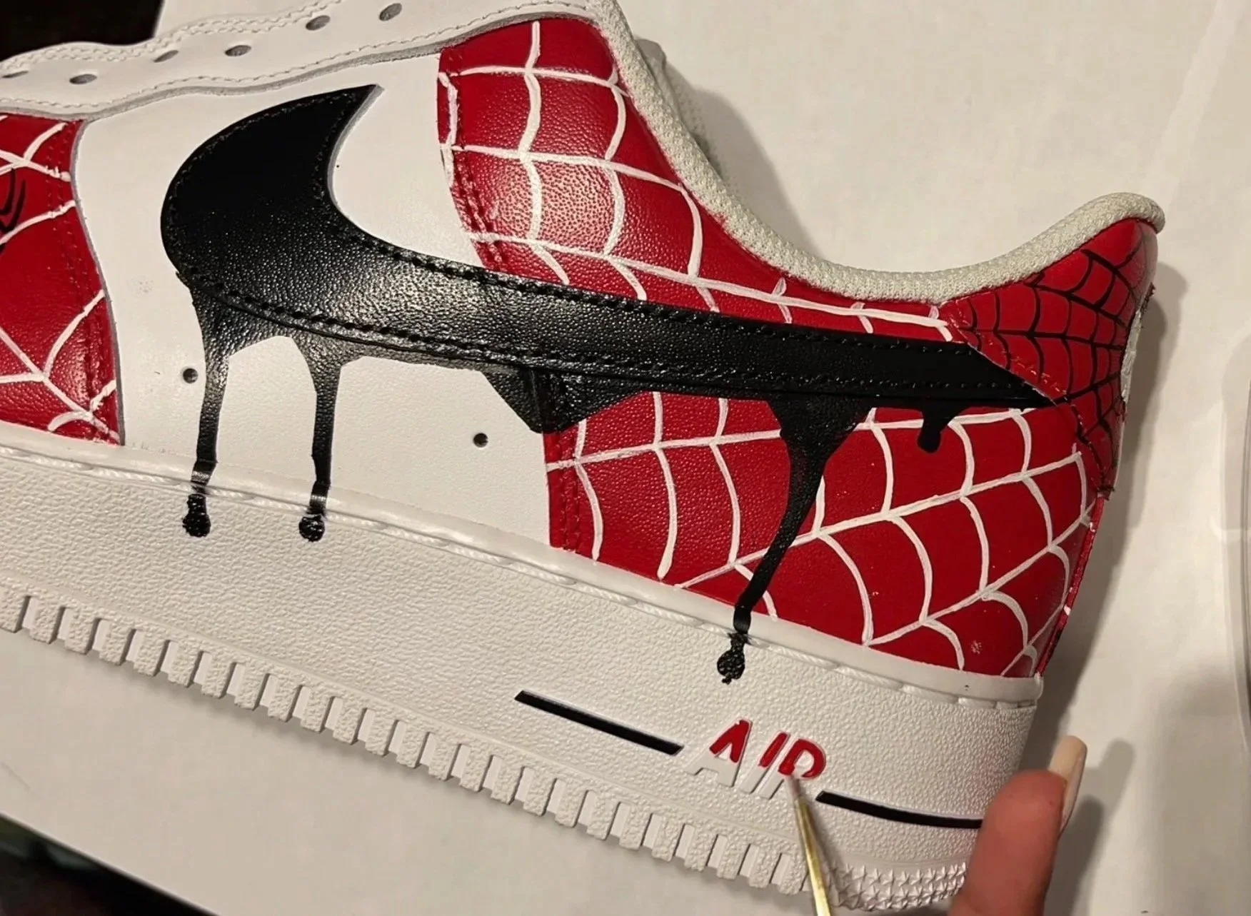 Close-up of a custom Spider-Man Nike Air Force 1 showing hand-painted web details and a black drip swoosh.