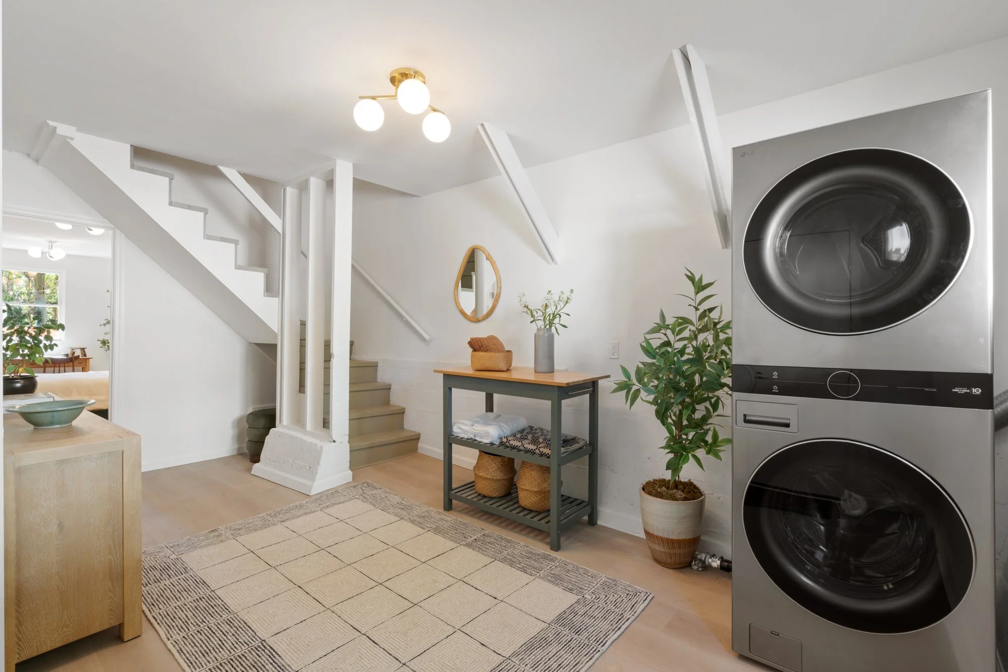 A laundry room with a stacked washer and dryer, a green table with baskets underneath, and decorative plants.