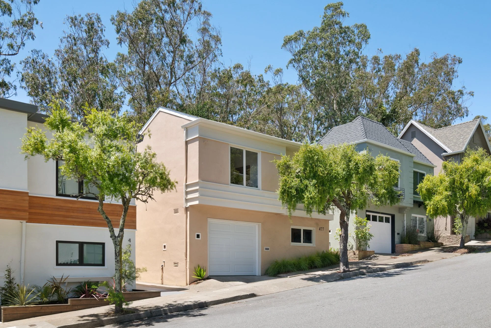 Row of modern residential houses with trees in front and a clear blue sky.