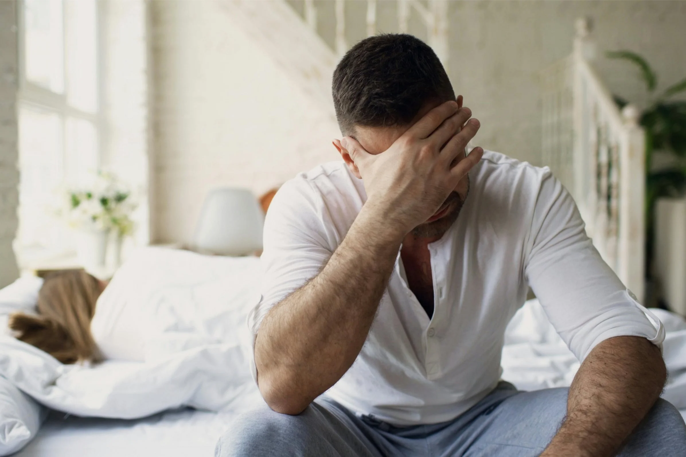 Man sitting on the edge of a bed with his head in his hand