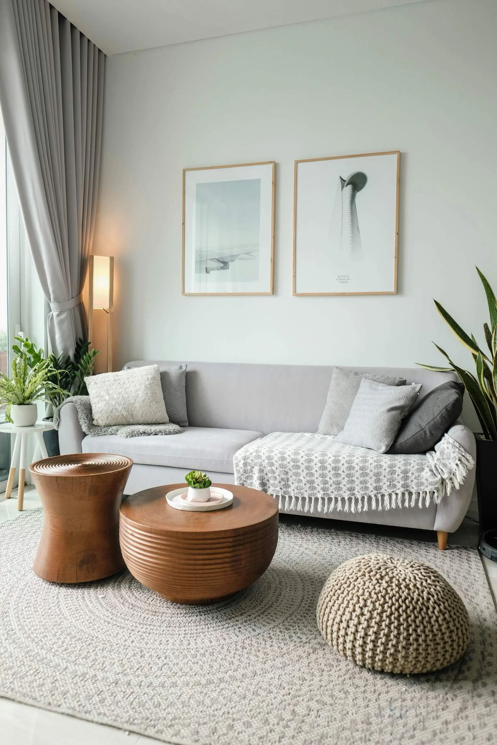 Calm, neutral-toned living room with a grey sofa, round wooden coffee table, woven rug, and framed prints on the wall