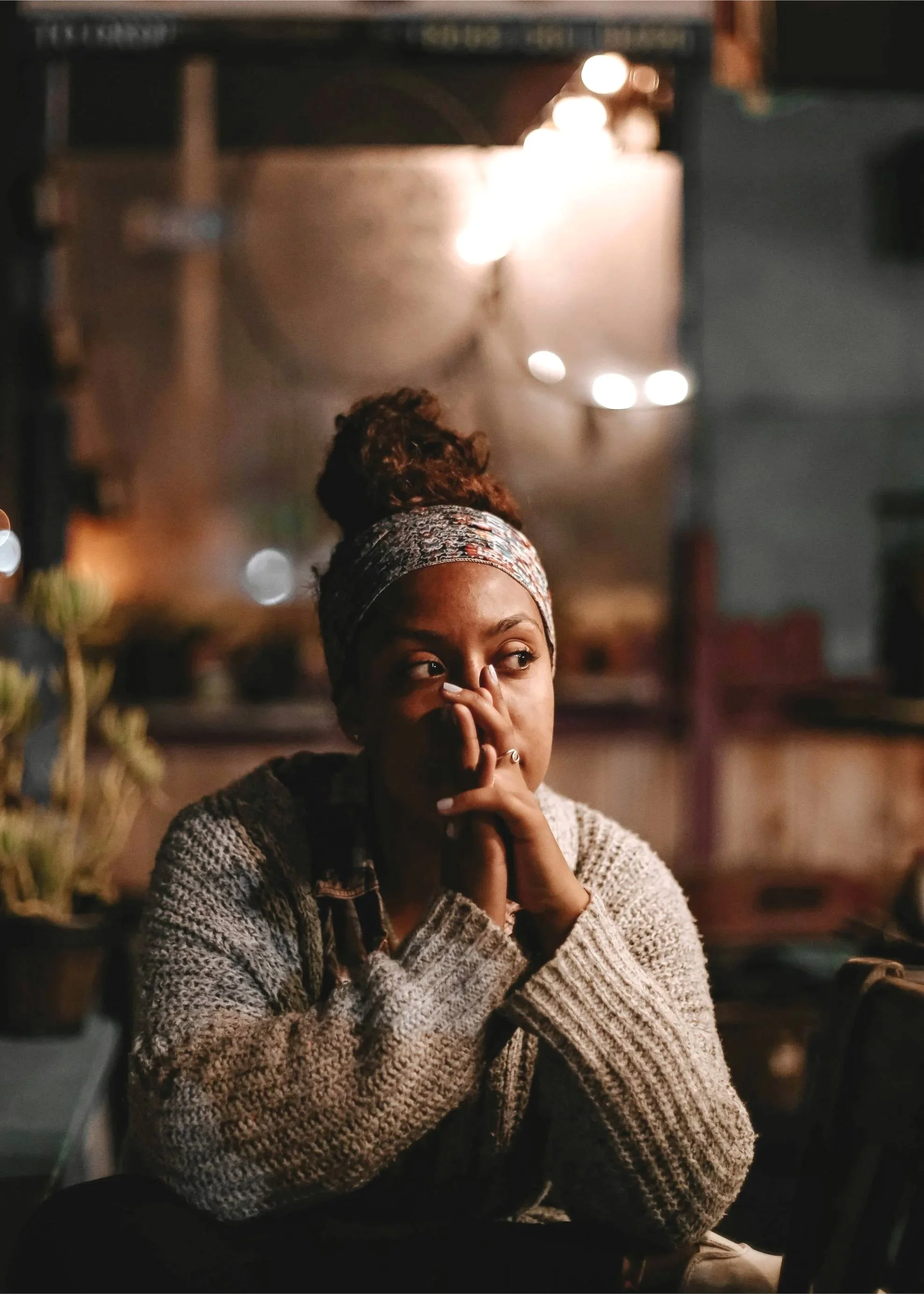 Woman sitting alone in a warmly lit room, looking pensive