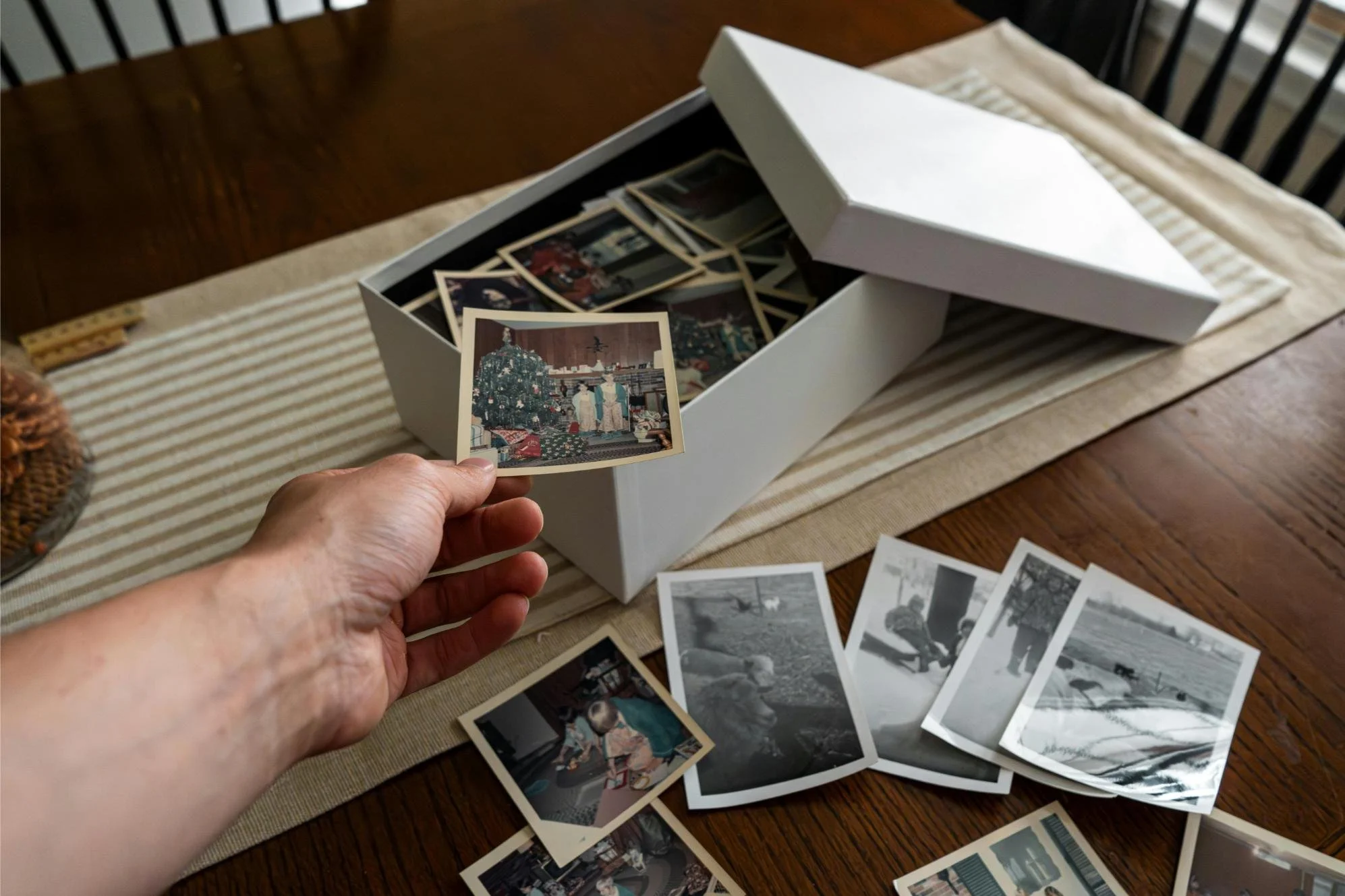 Hand lifting an old family photograph from a box of scattered vintage prints on a table