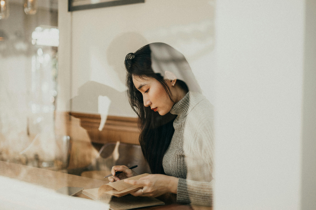 Woman journaling thoughtfully by a window in warm light