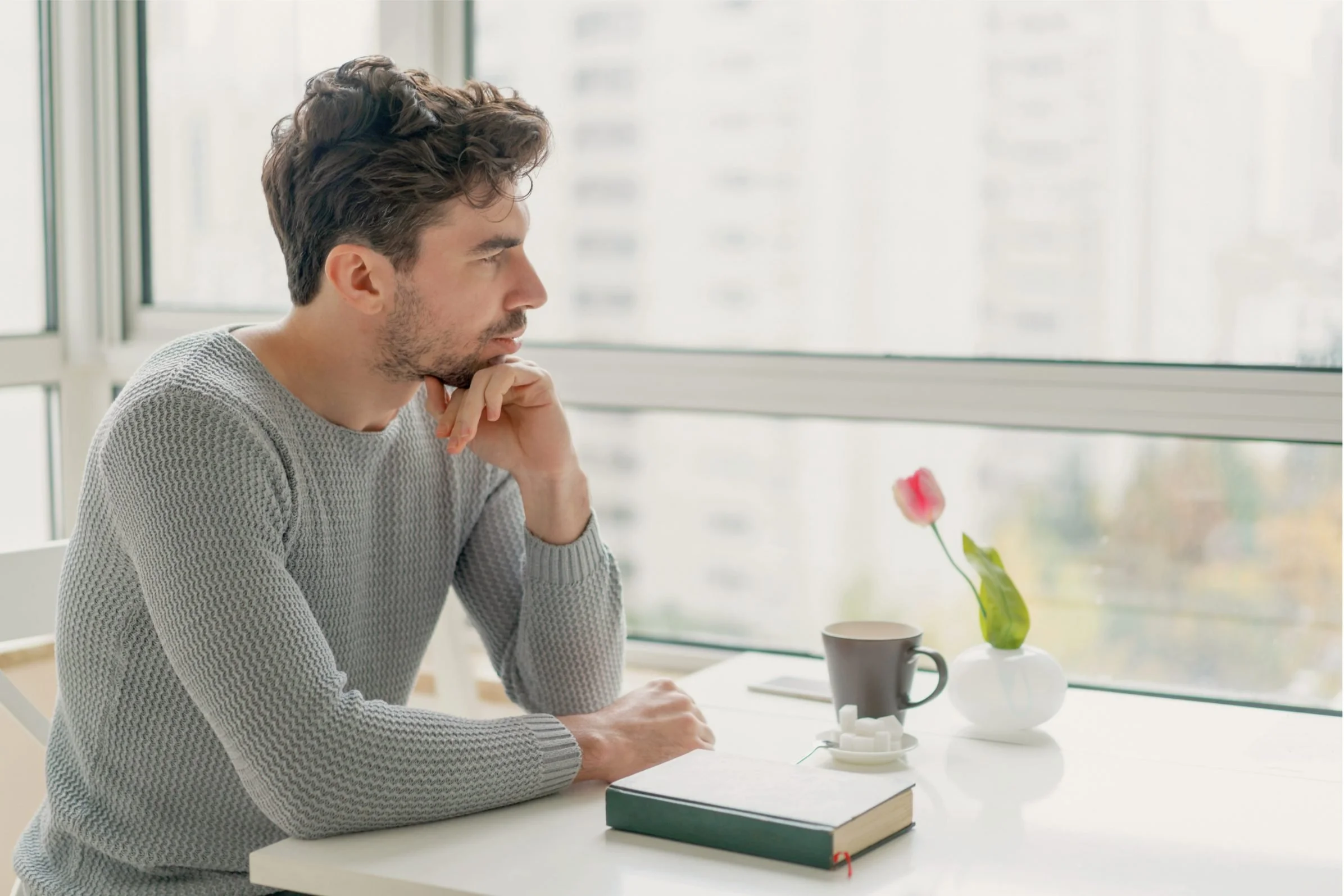 Man sitting by a window, looking thoughtful and reflective