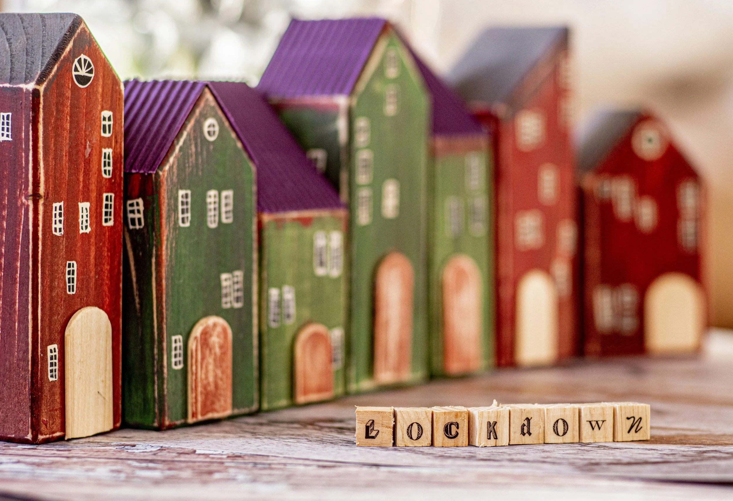Colorful wooden houses with painted exteriors and white window details, placed on a shelf, with wooden alphabet blocks spelling 'lockdown' in front.